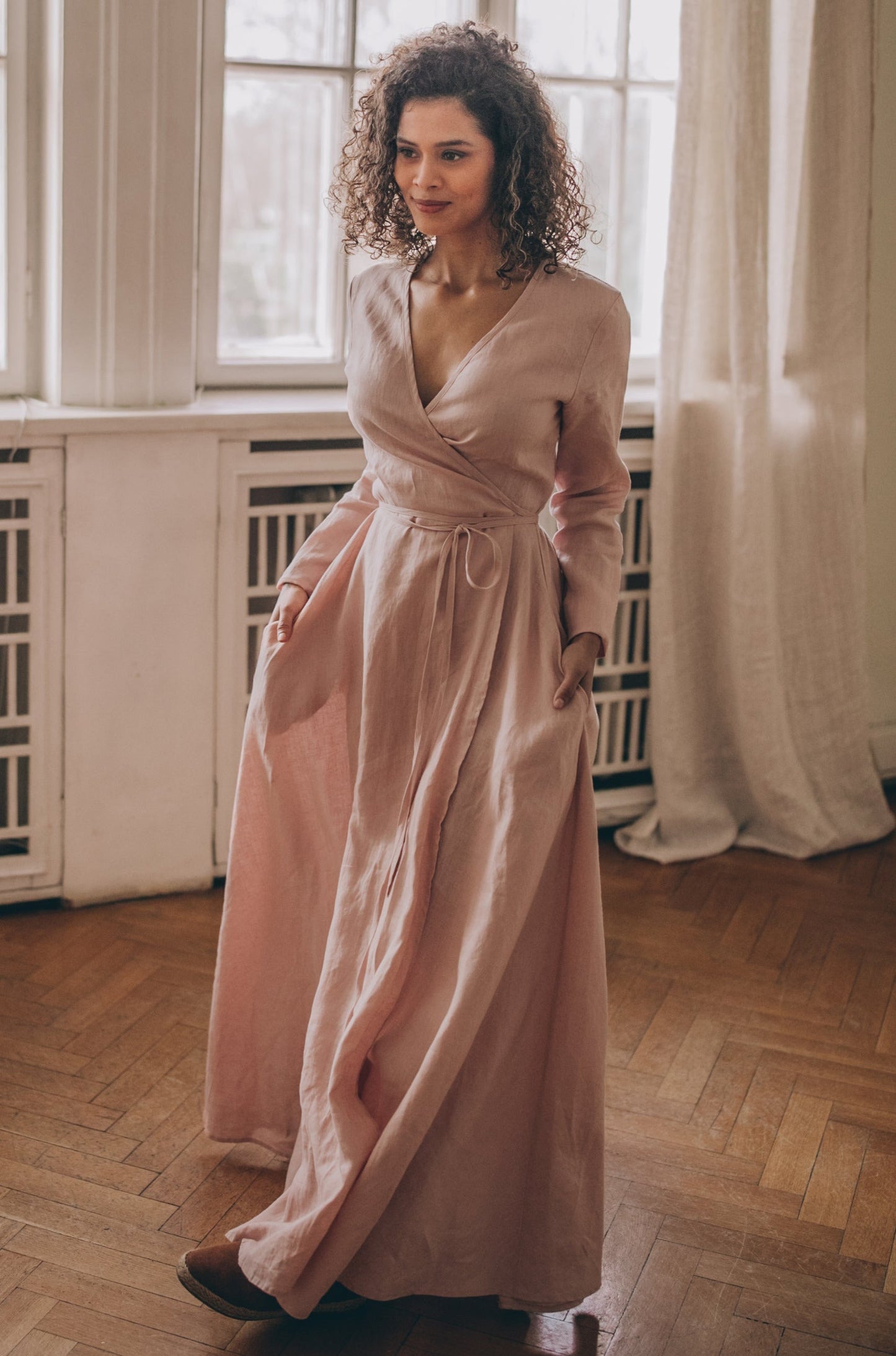 Woman wearing blush linen maxi dress with tie waist and V-neck in bright room