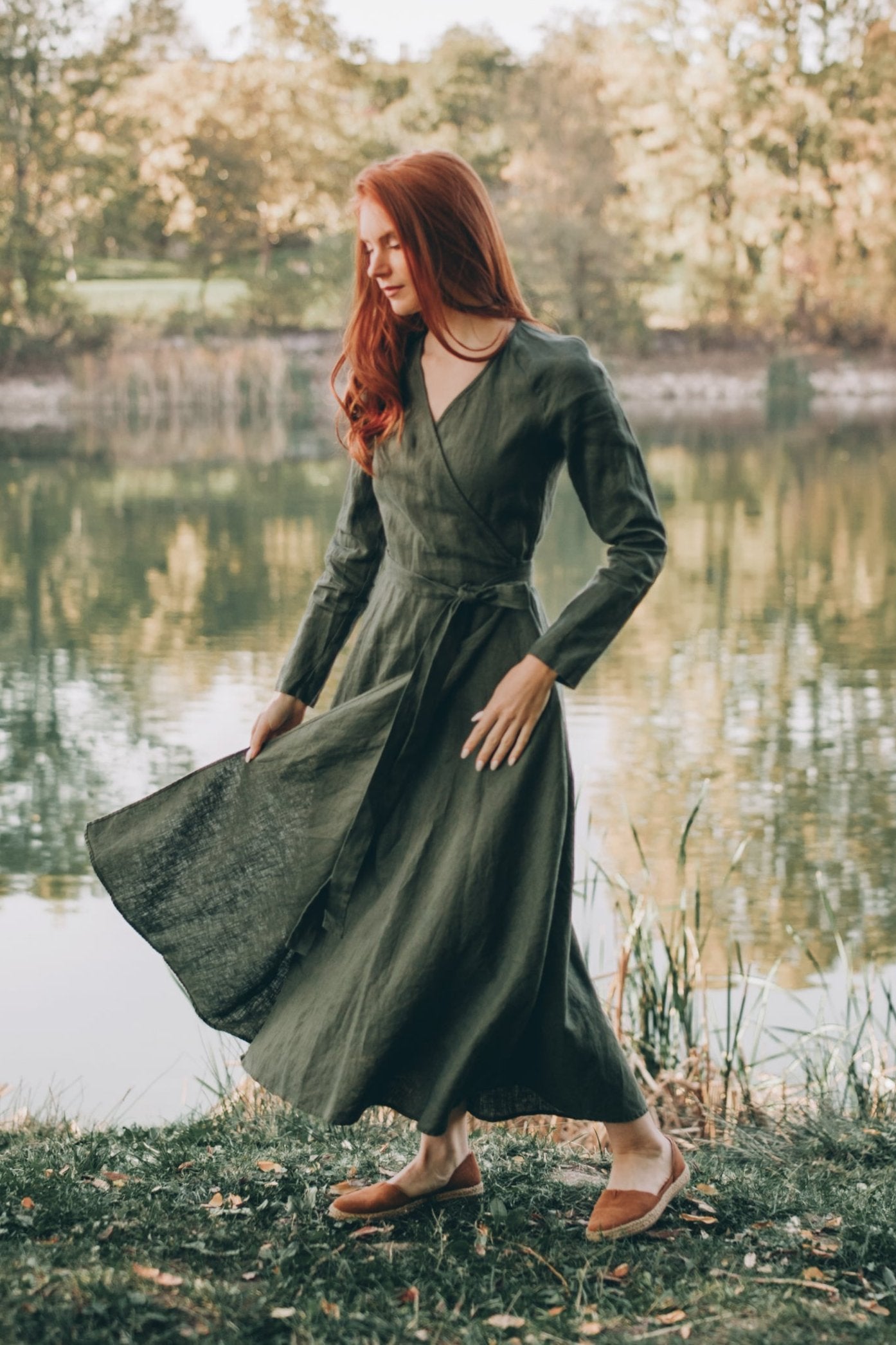 Woman wearing long sleeved linen midi wrap dress by a lake in autumn setting