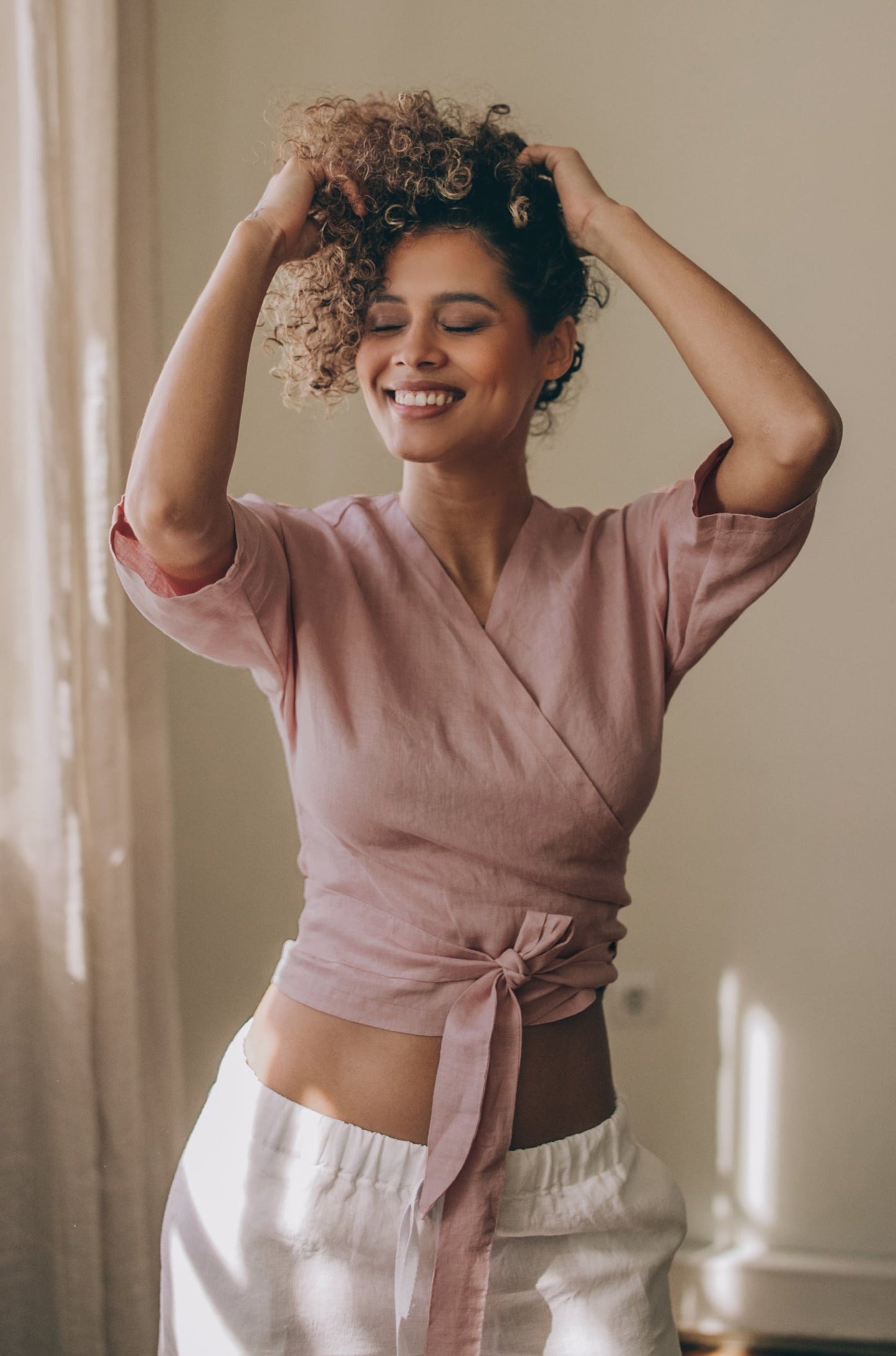 Woman wearing blush minimalist linen wrap top with tie closure and elbow-length sleeves