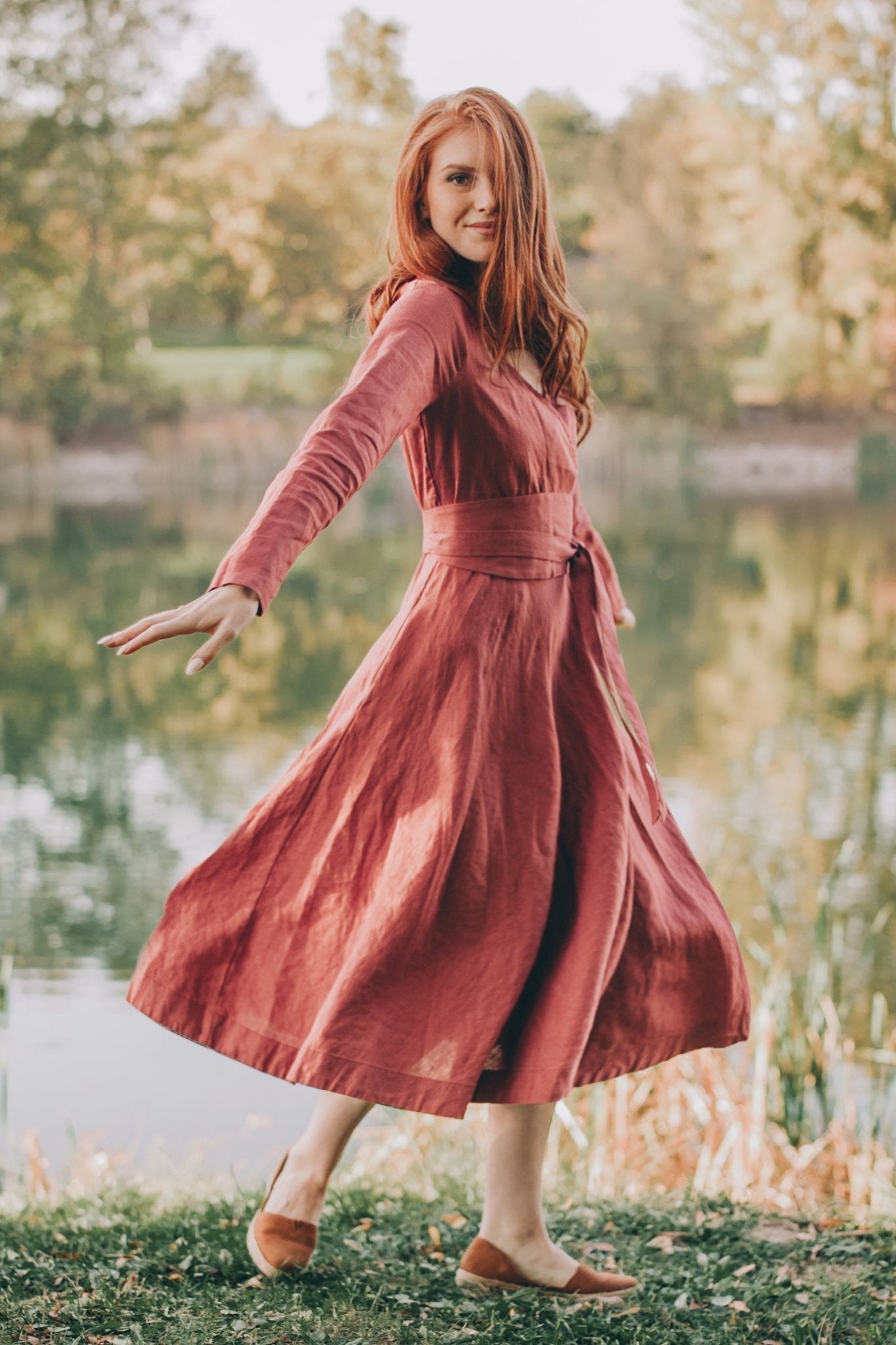 Woman wearing a red linen midi dress with tie belt standing near a lake outdoors
