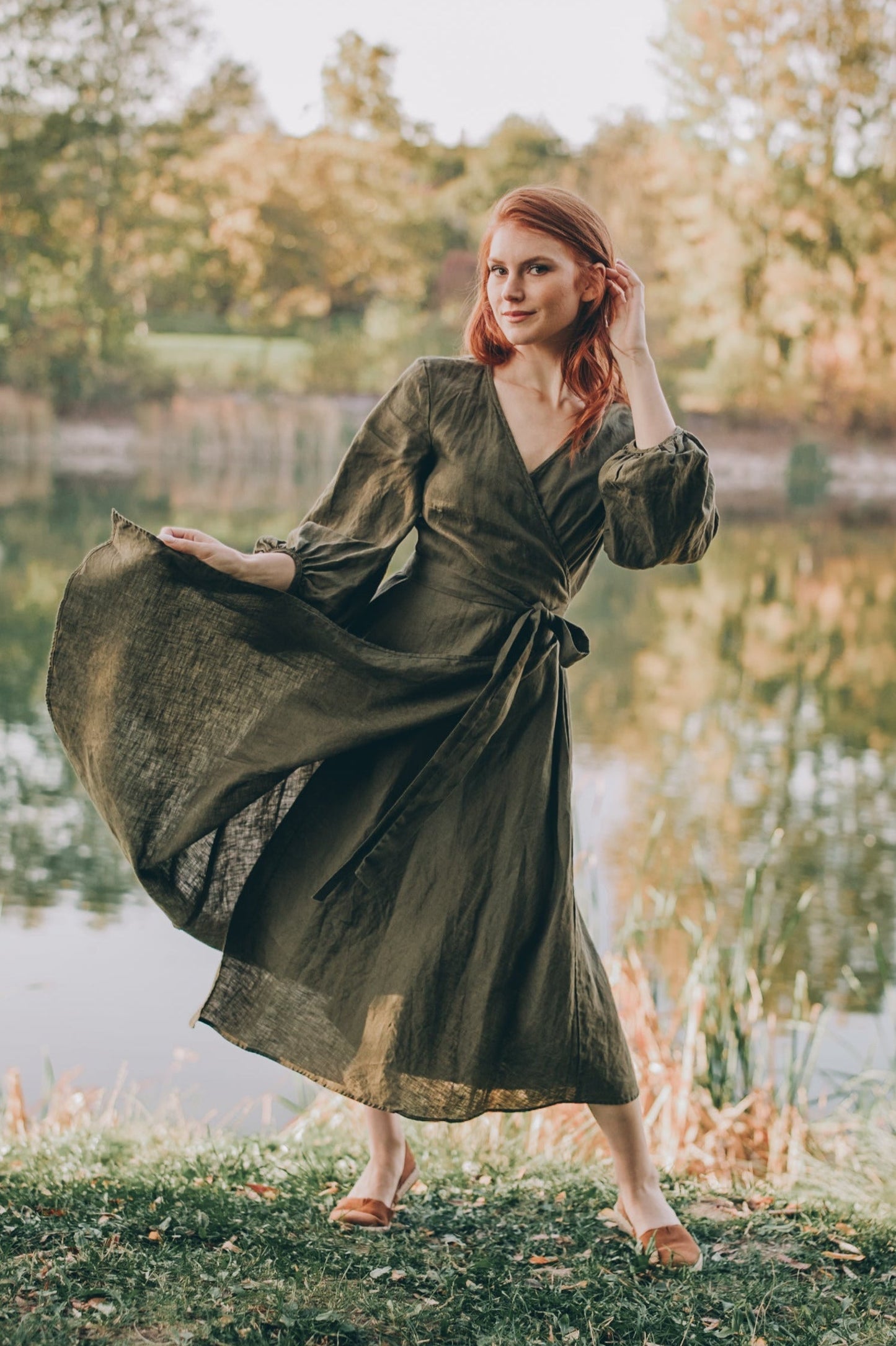 woman wearing green linen wrap dress with puff sleeves and tie waist standing outdoors near water
