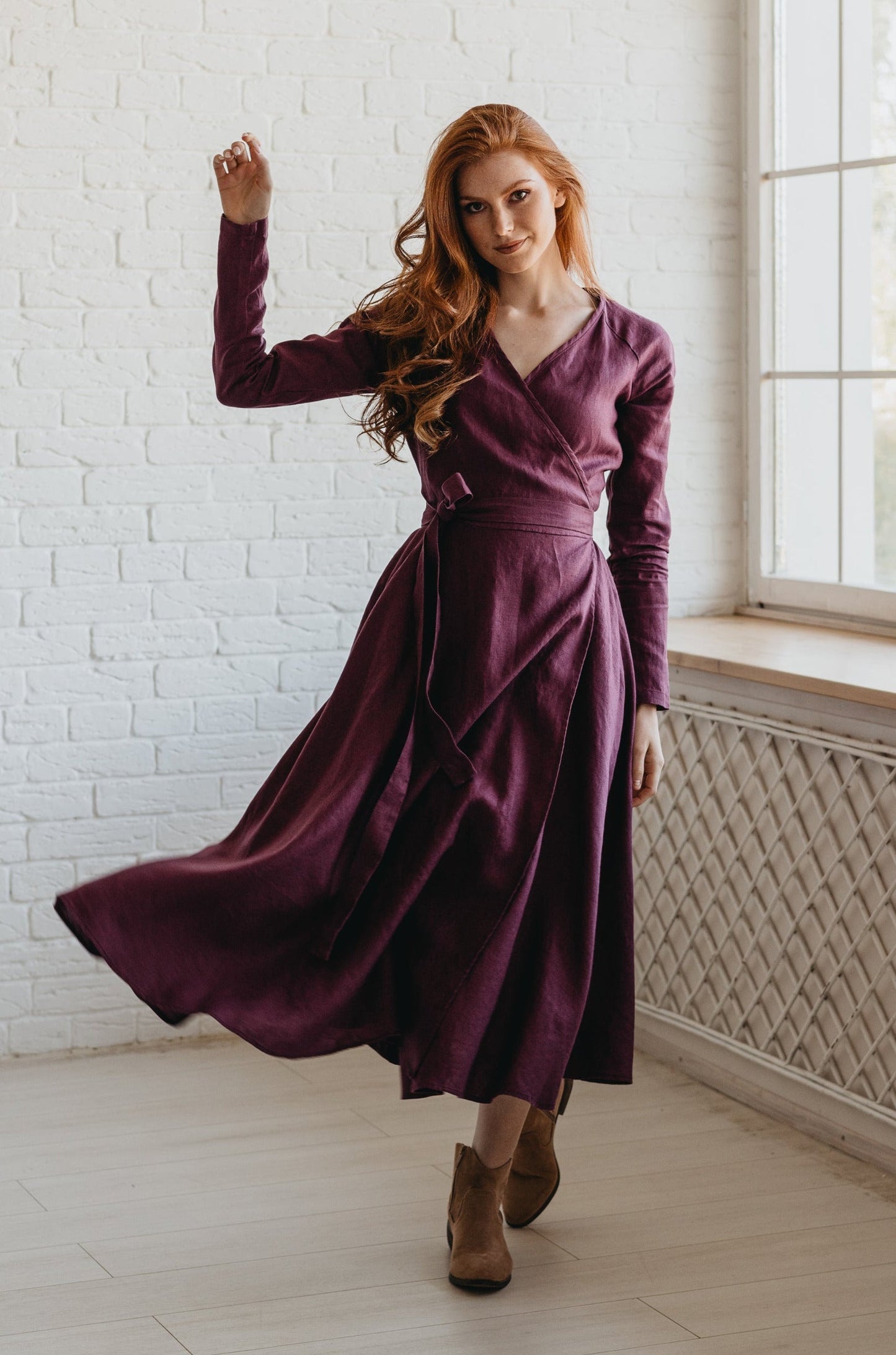 Woman wearing plum linen A-line midi dress with tie waist and V-neck standing by window