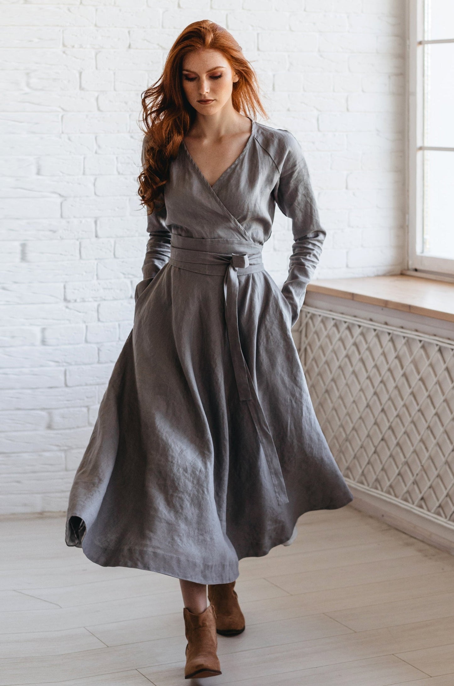 Woman wearing gray heavyweight linen dress midi length with wrap top, V-neckline, side pockets, and wide tie belt