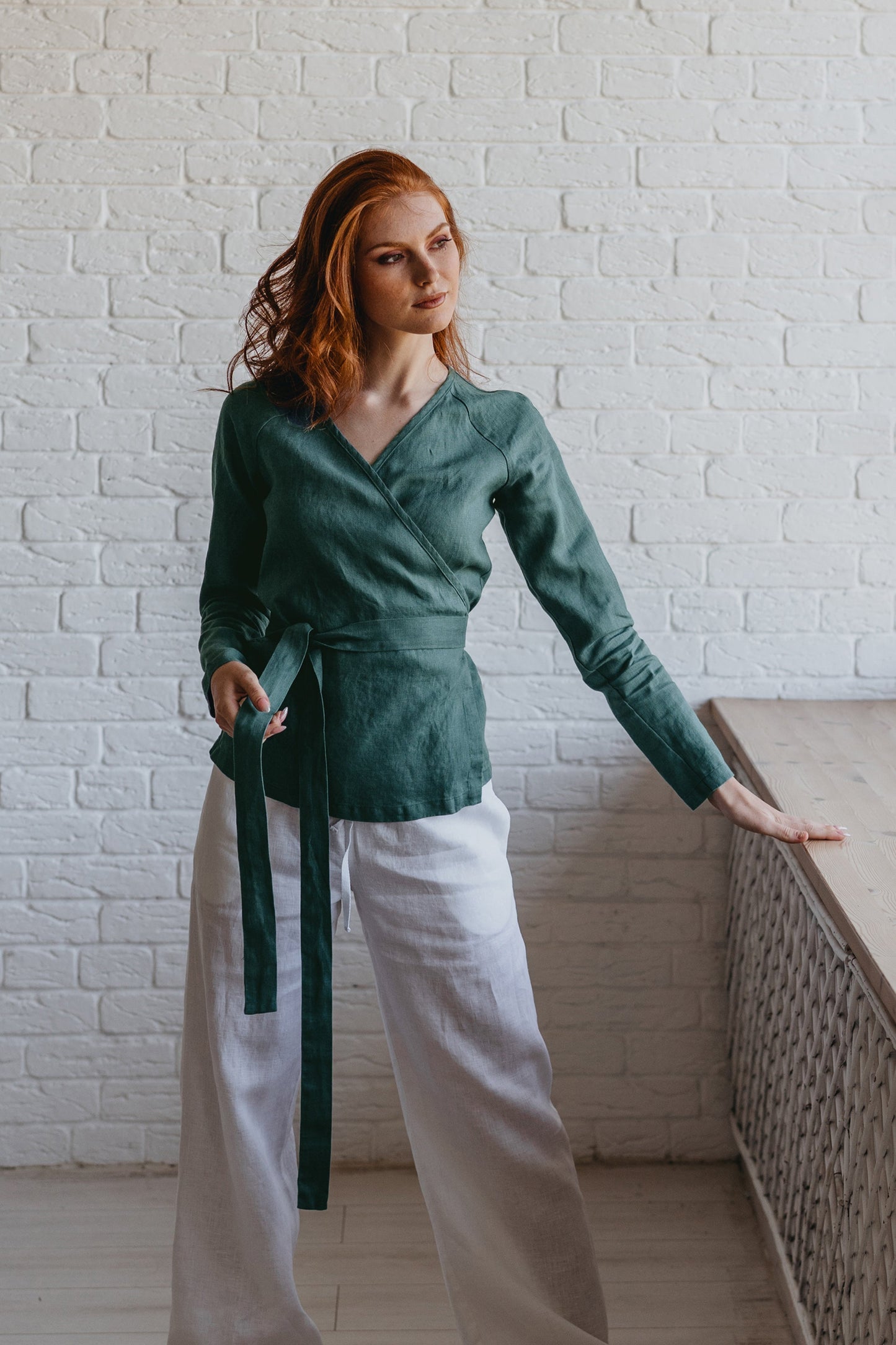 Woman wearing elongated minimalist linen wrap top with long sleeves and tie closure in green