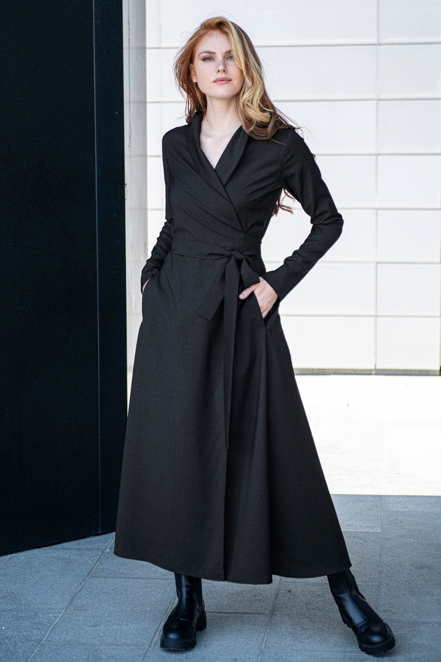 Woman wearing black wool wrap dress with shawl collar and side pockets, styled with black boots