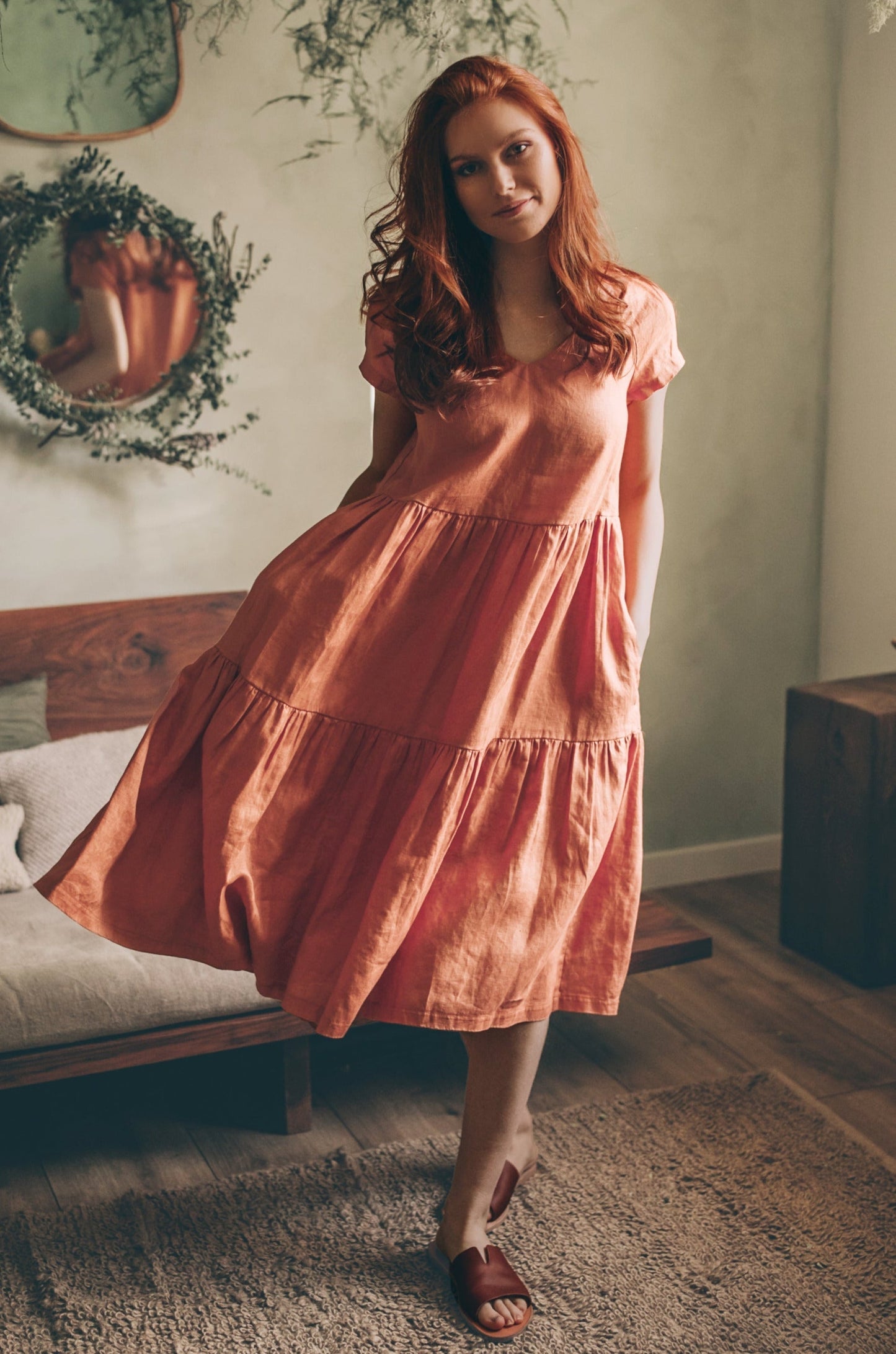 Woman wearing rusty orange bohemian linen dress midi length with short sleeves and tiered skirt indoors