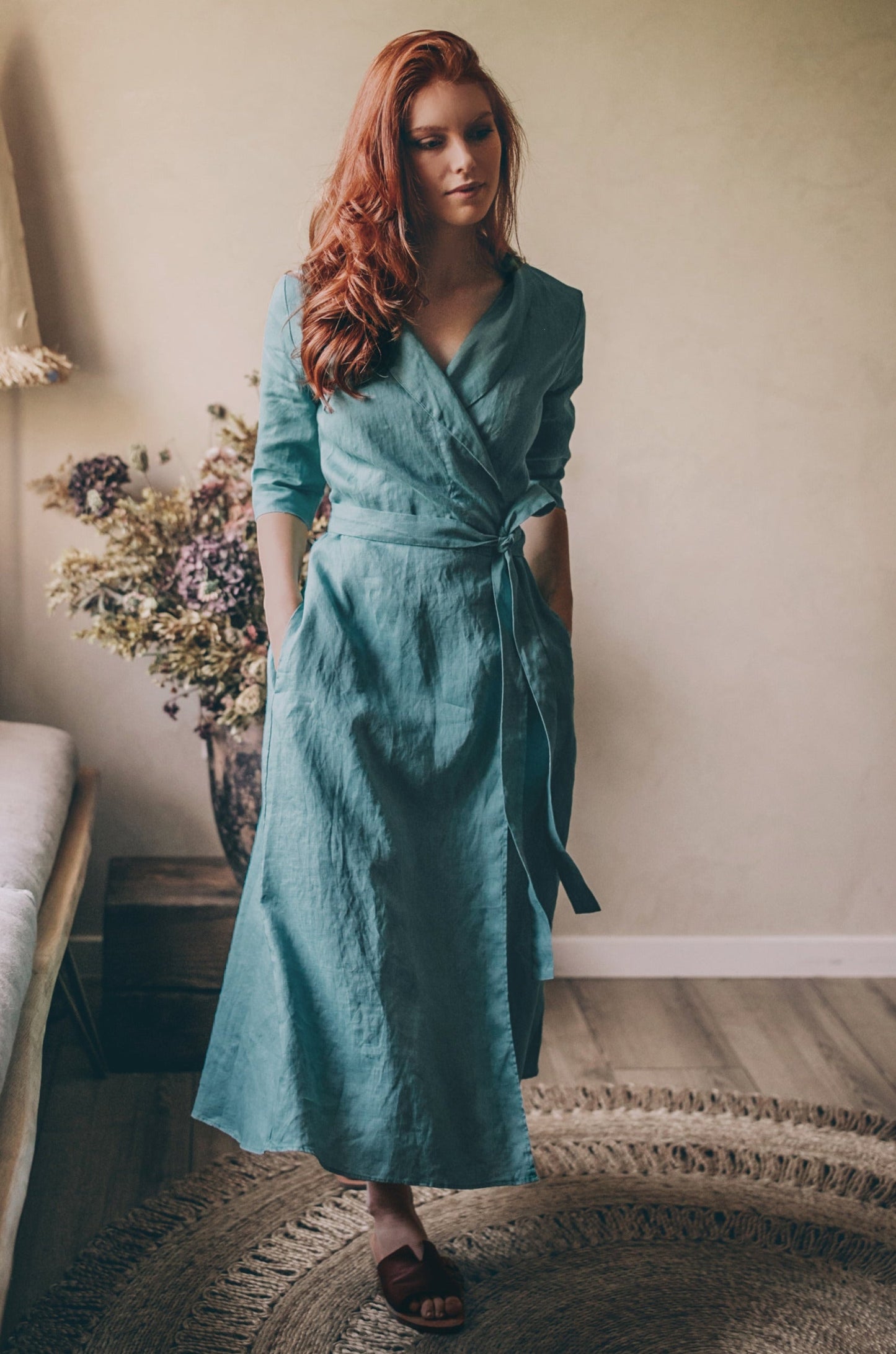 Woman wearing teal midi length linen dress with tie waist standing indoors