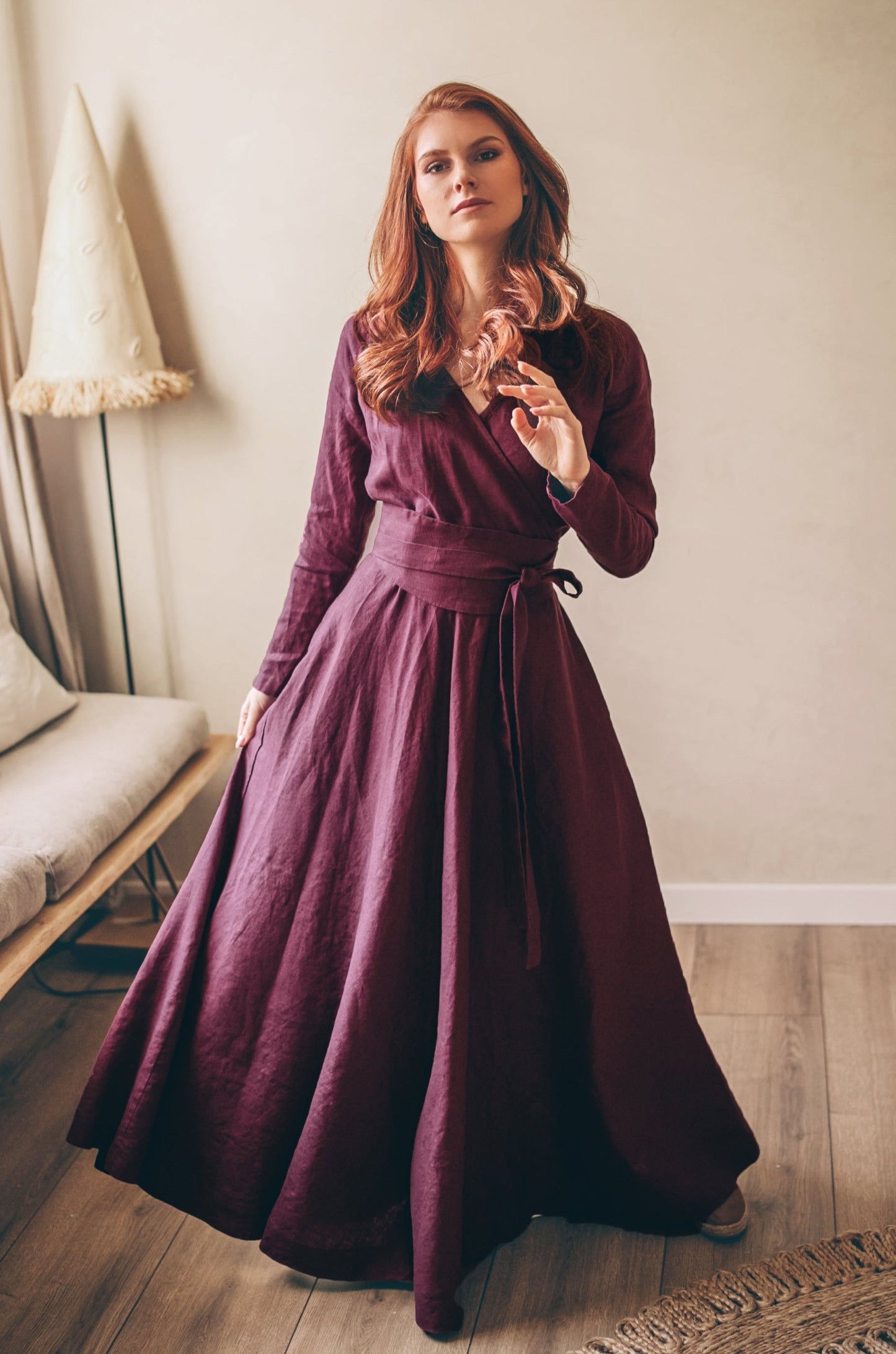 Woman wearing plum heavy linen wrap dress with waist belt and long sleeves indoors