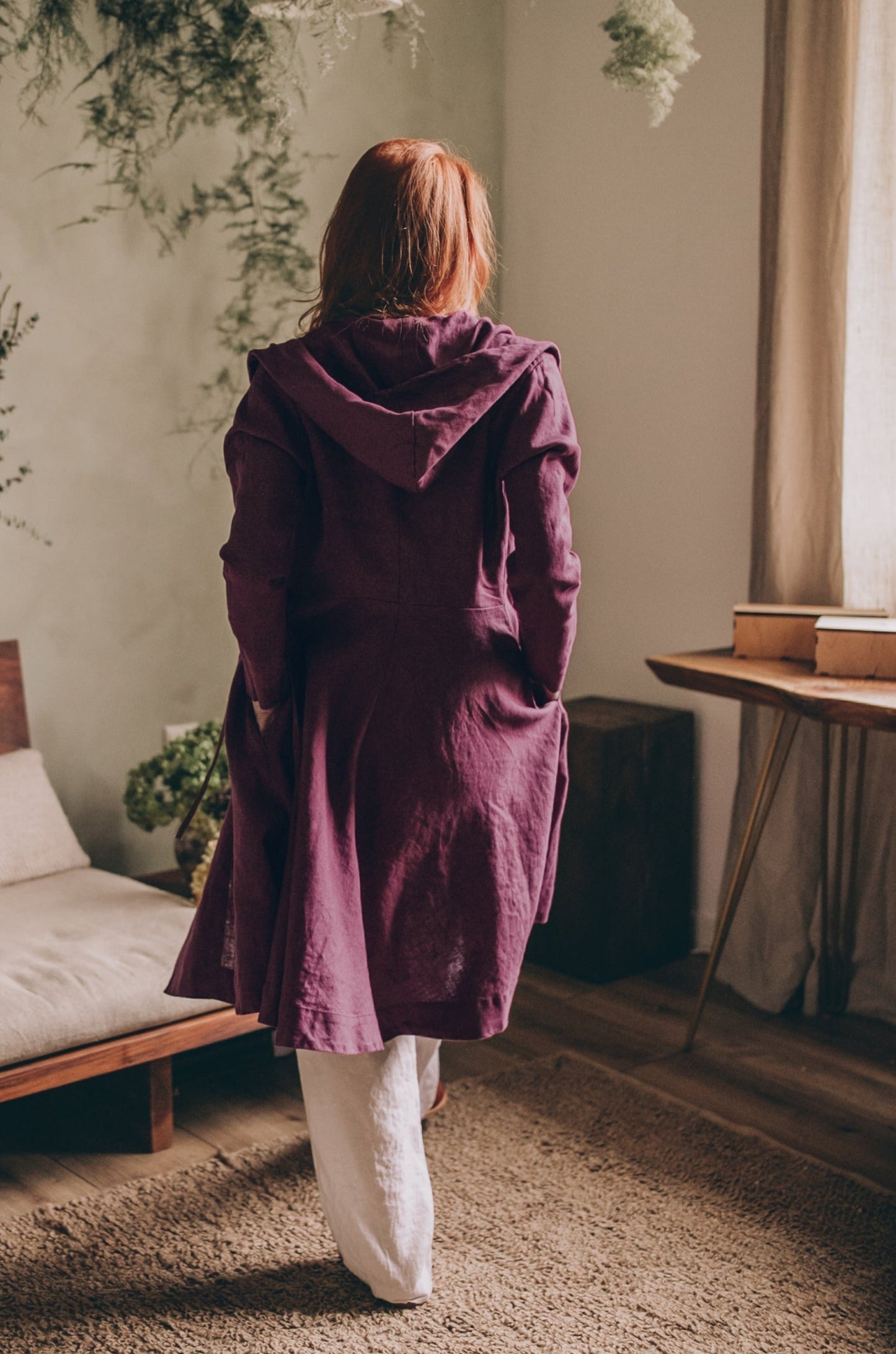 Woman wearing purple midi length summer linen coat with hood and tie closure indoors
