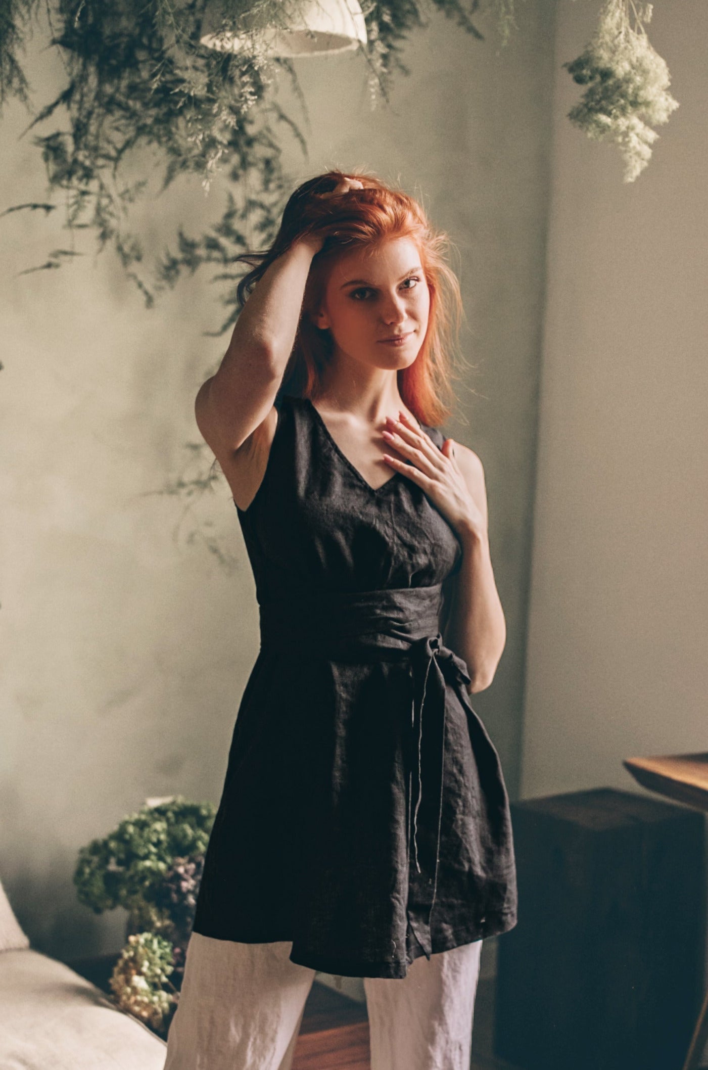 Sleeveless linen tunic top with tie belt in black worn by woman indoors