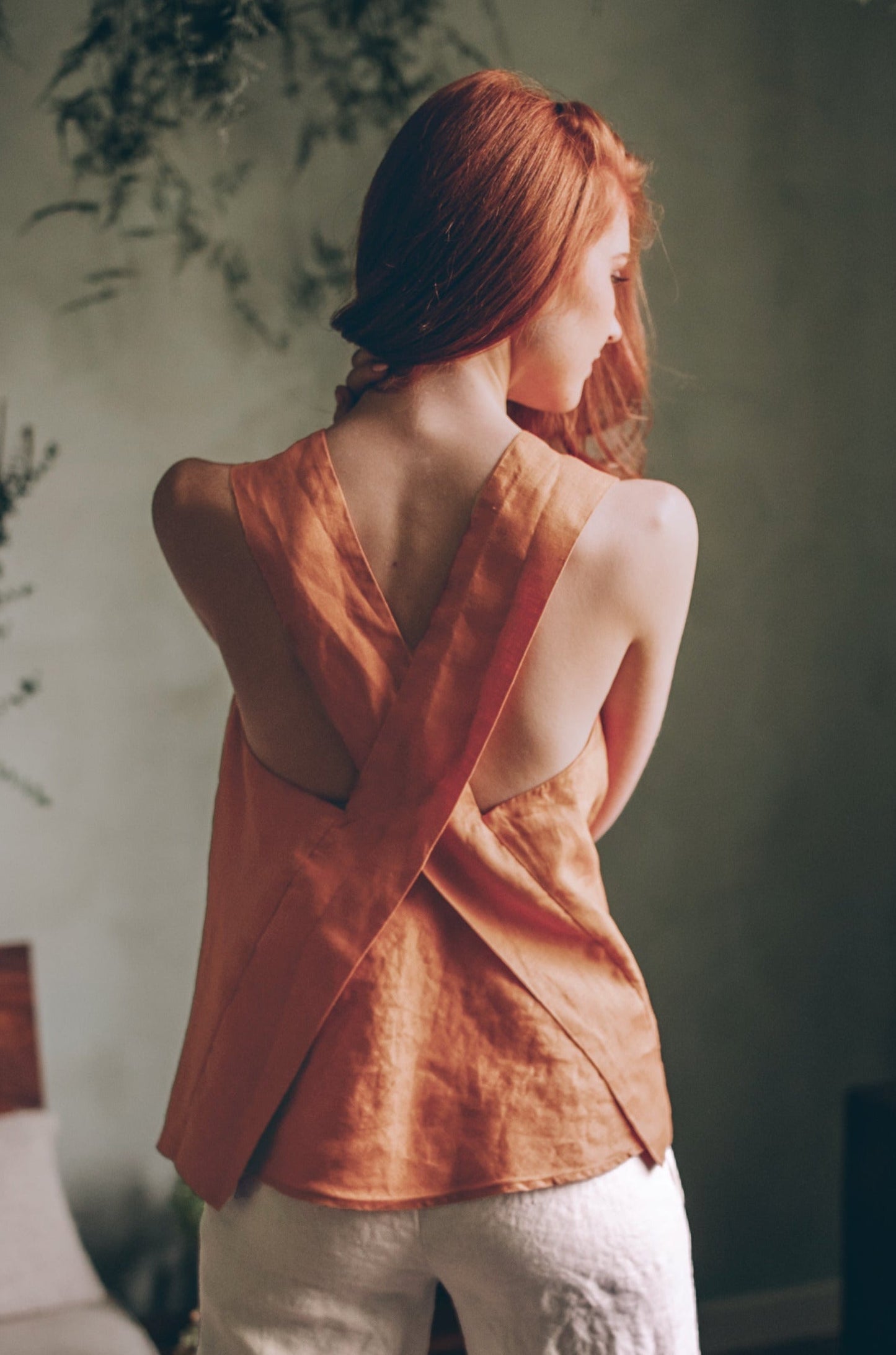 Woman wearing rust-colored cross-back linen top paired with white bottoms in soft natural light