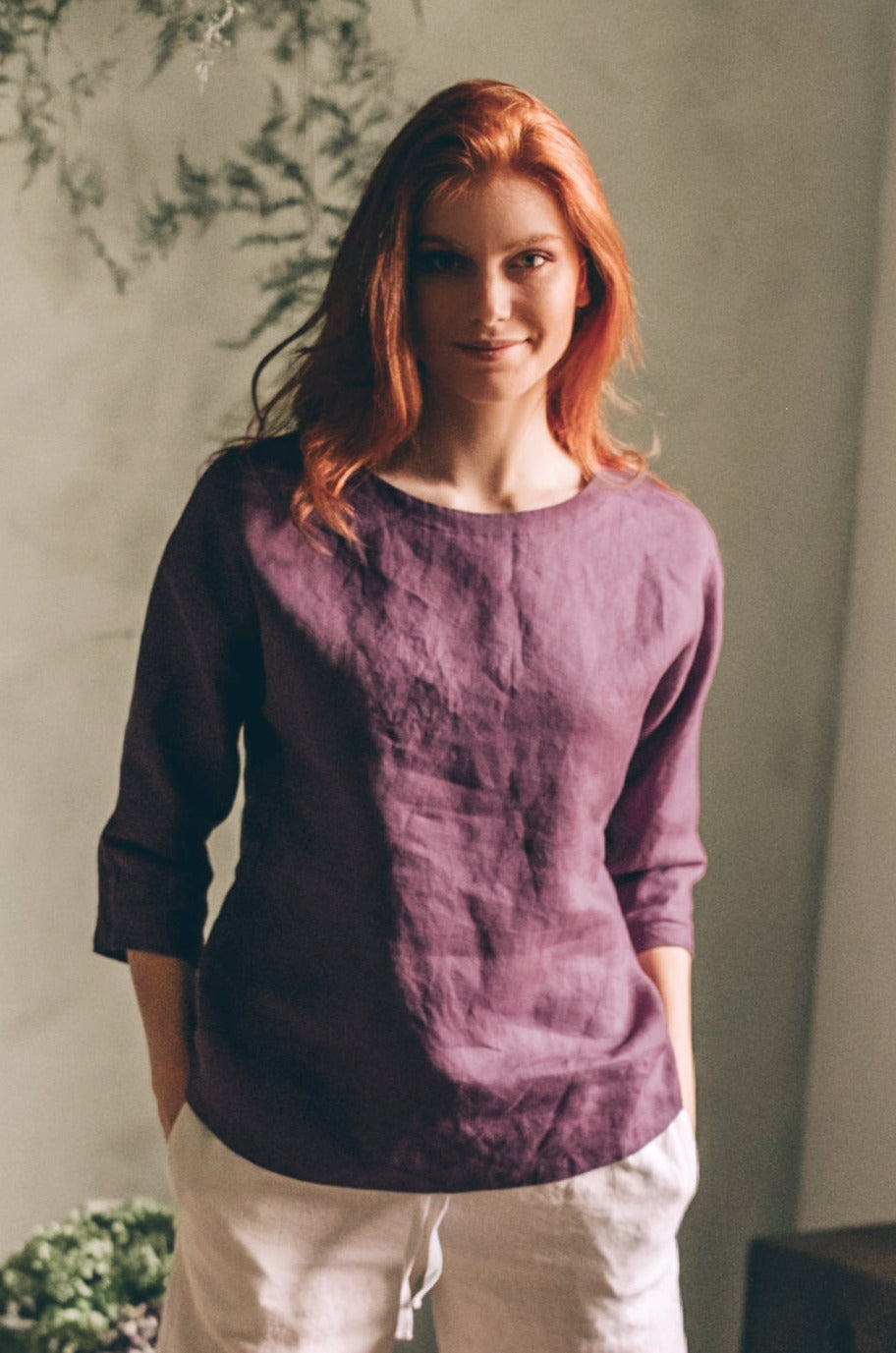 Woman wearing purple essential linen blouse with three-quarter sleeves and relaxed fit in natural light room