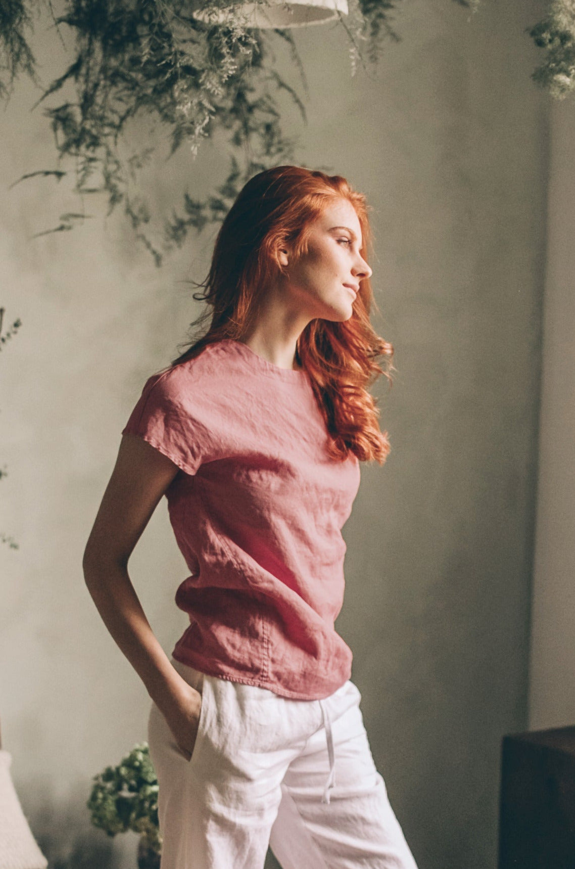 Woman wearing pink linen shirt top with stitched detailing and white pants indoors