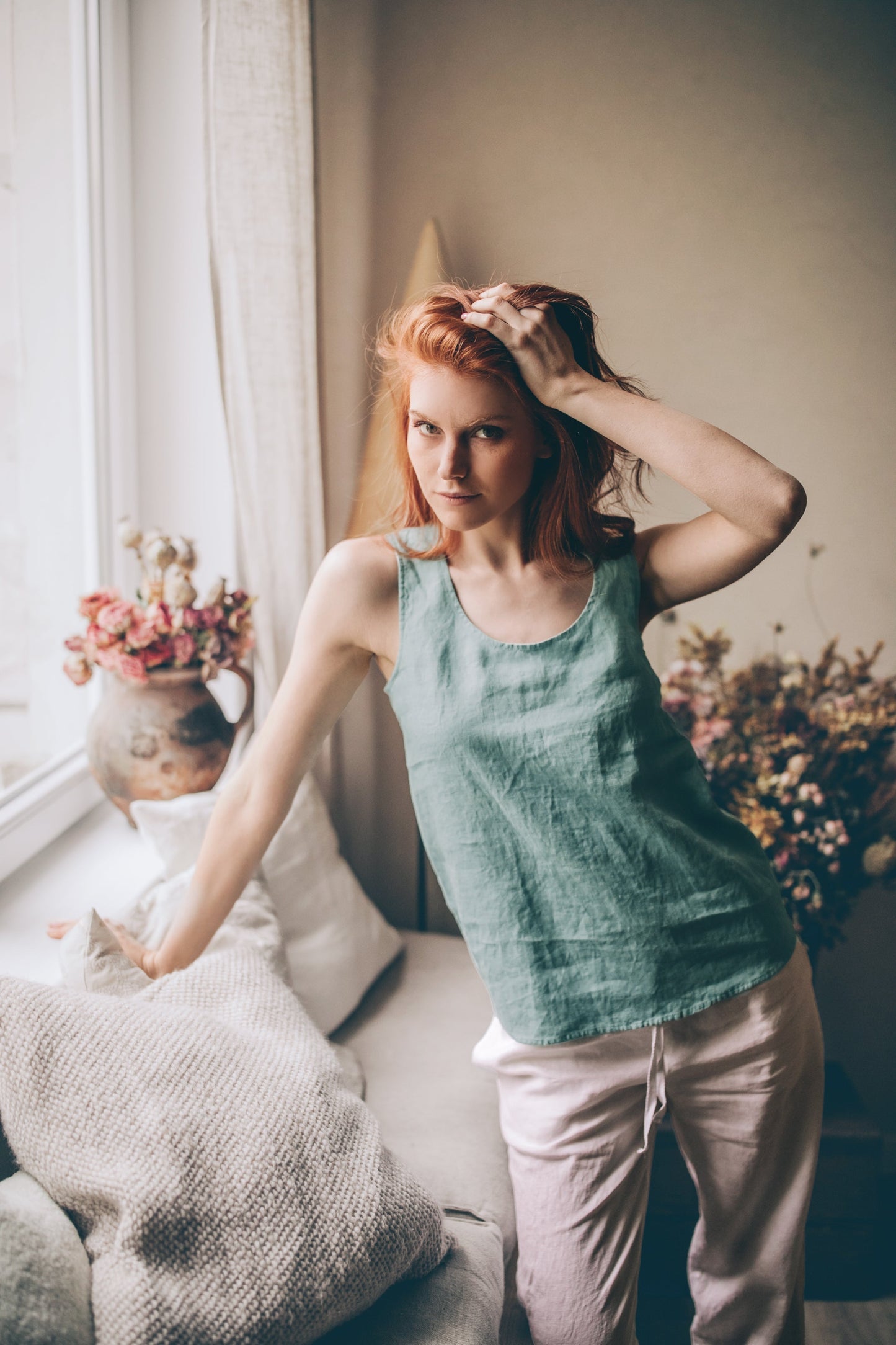 Woman wearing a green linen tank top with scoop neckline in a cozy indoor setting
