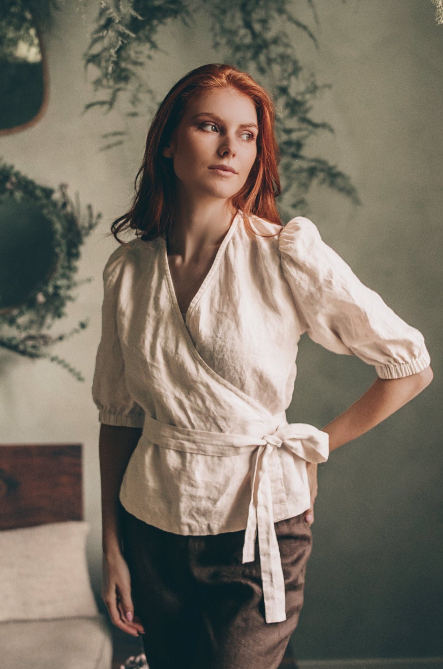 Woman wearing puff sleeve linen wrap top with tie belt in natural light indoors