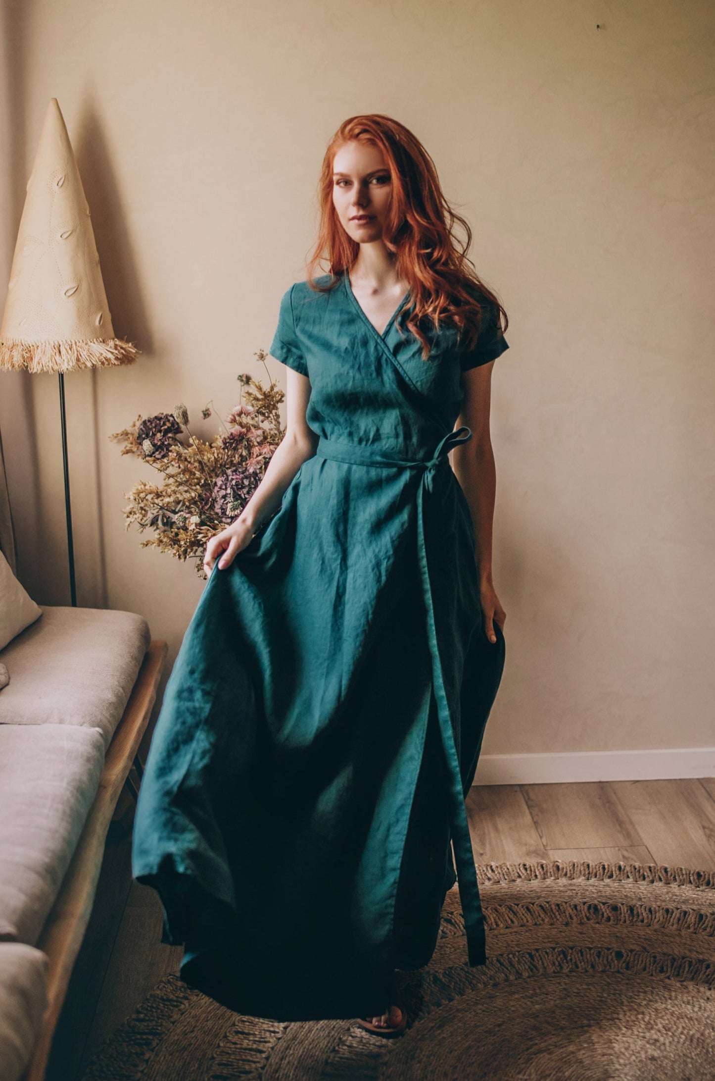 Woman wearing a short sleeve linen wrap maxi dress with tie waist in teal color indoors