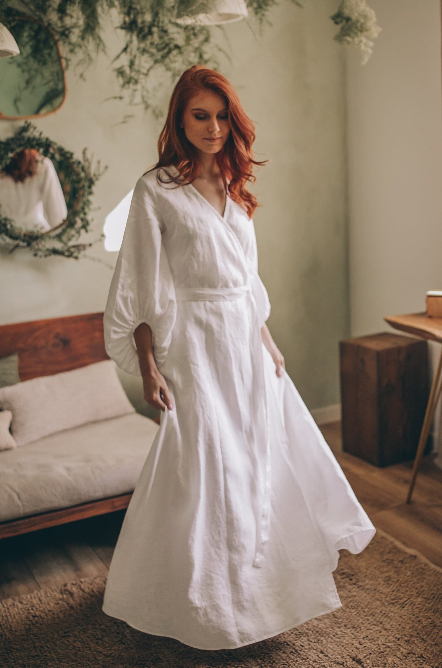 Woman wearing white linen maxi dress with puff sleeves and tie belt in cozy room