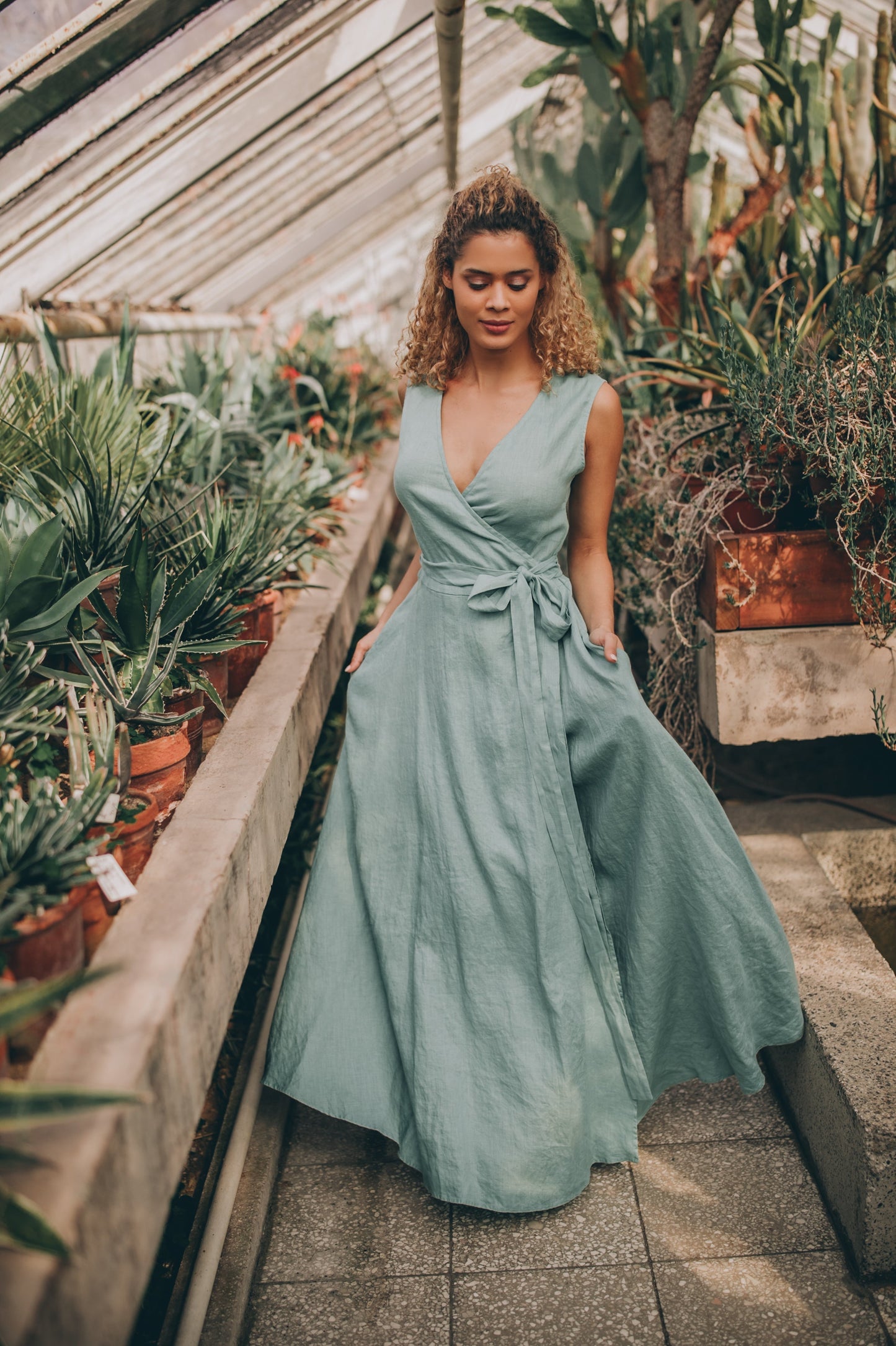 Woman wearing sleeveless linen maxi dress with tie waist in greenhouse setting