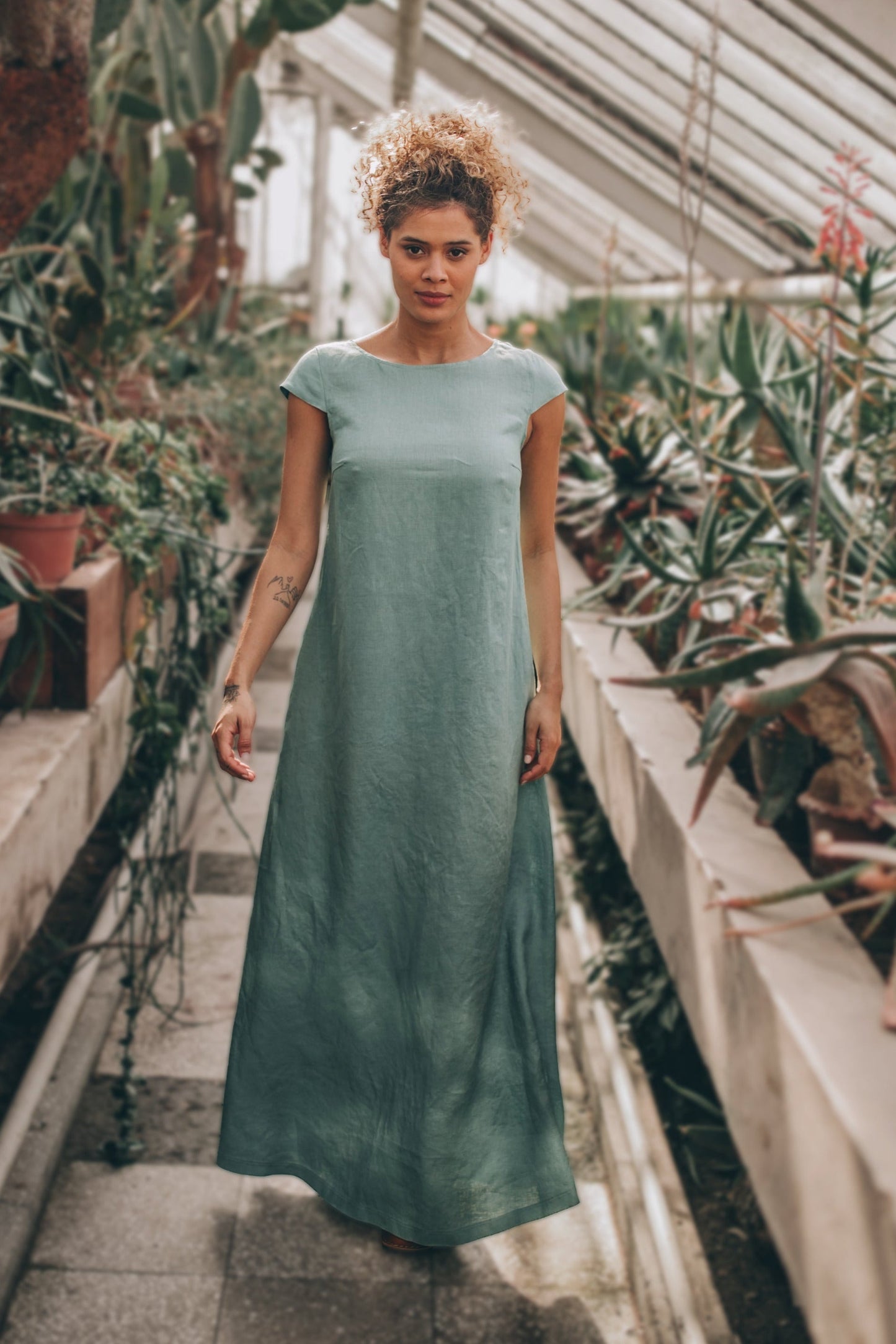 woman wearing gray linen maxi dress with cap sleeves standing in greenhouse