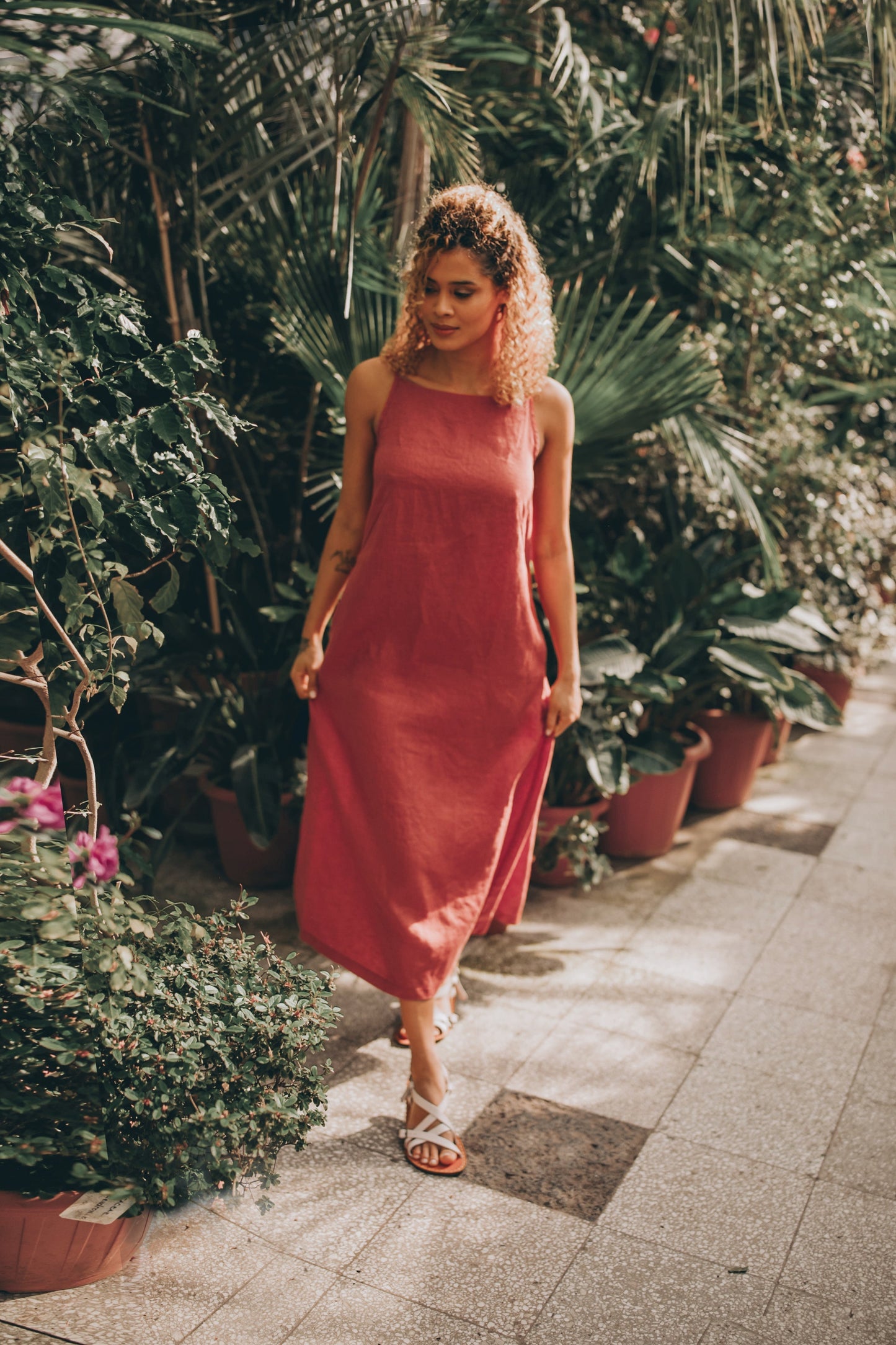 Woman wearing sleeveless linen midi dress walking outdoors among plants