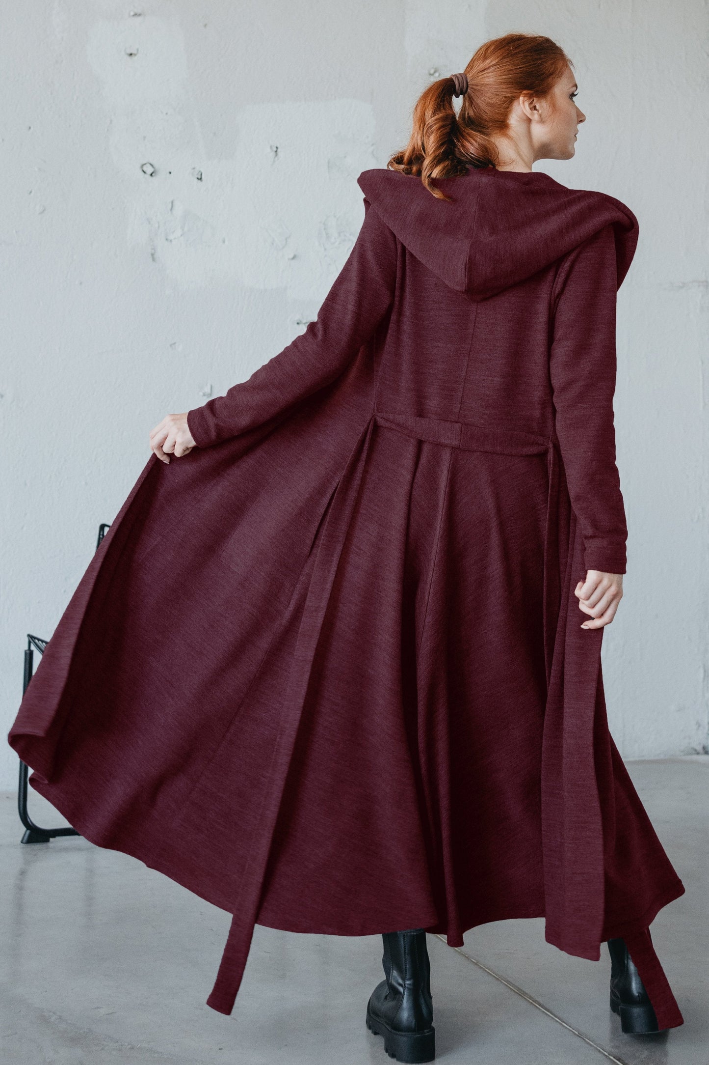 Woman wearing a burgundy long hooded cardigan with a flared design and matching belt, standing indoors