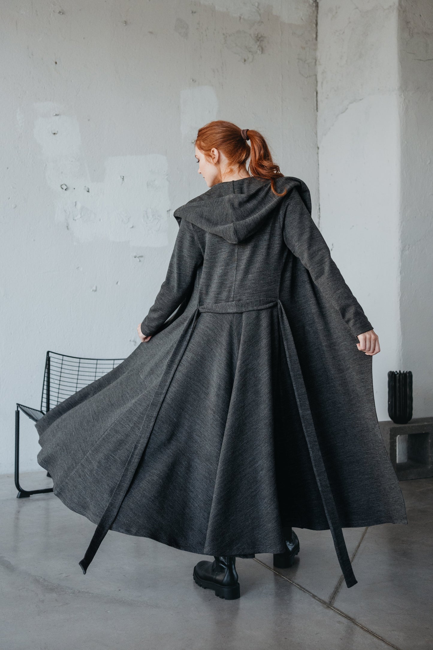 woman wearing long dark gray hooded cardigan with flared design and belt indoors