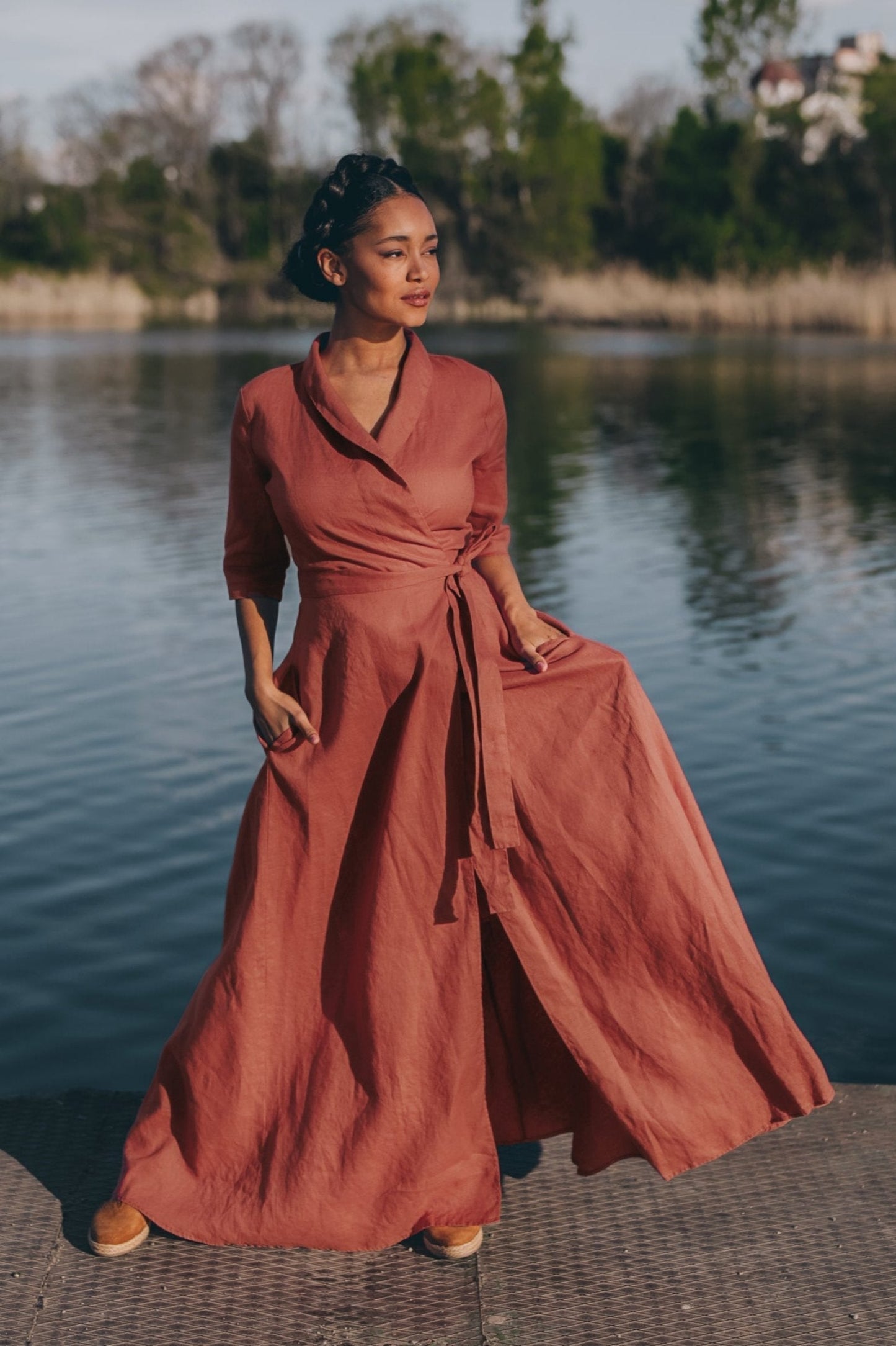 Woman wearing rust-colored linen A-line dress with tie waist standing by water
