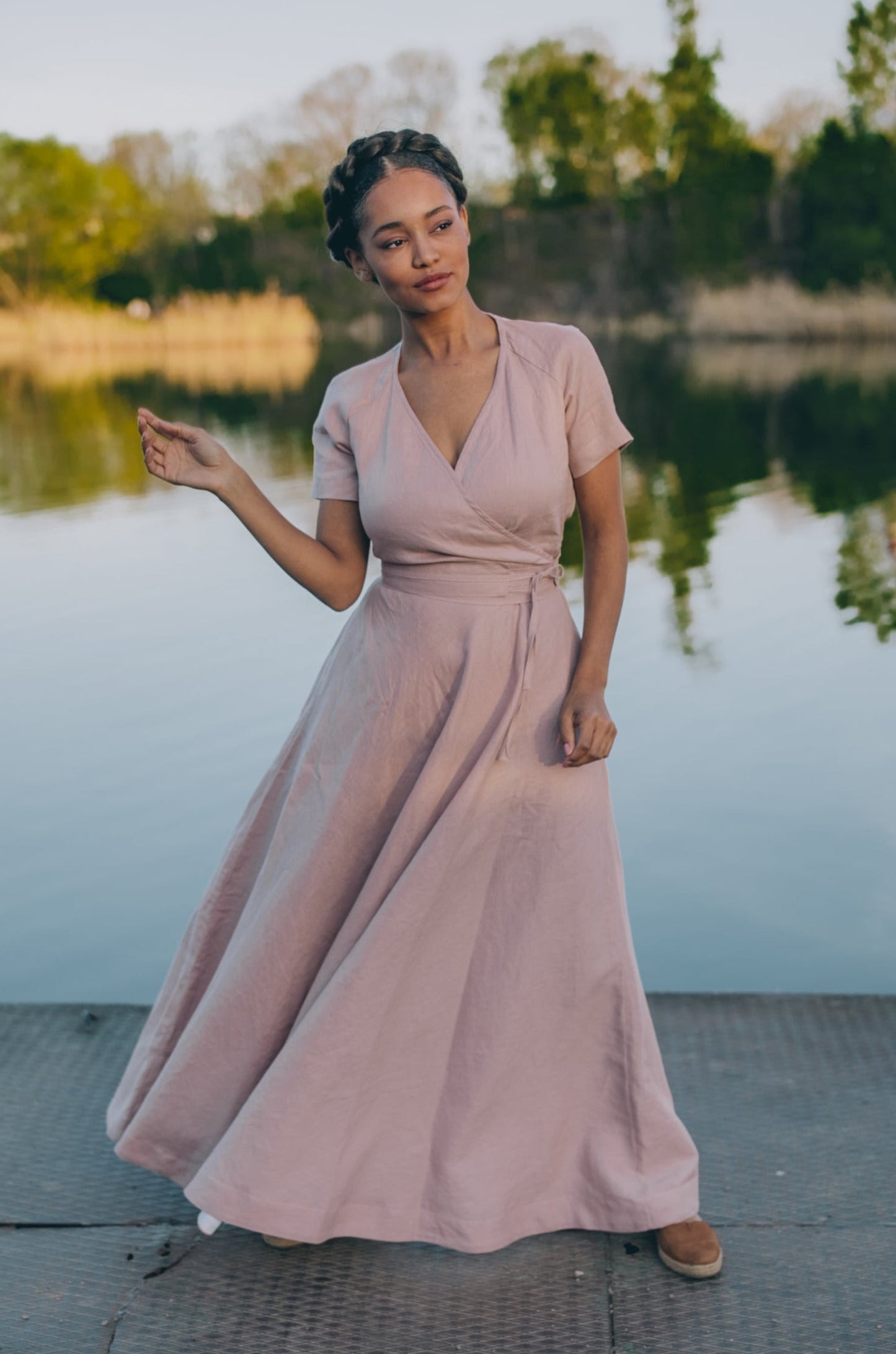 Woman wearing blush linen wrap dress with short sleeves and surplice neckline near lake