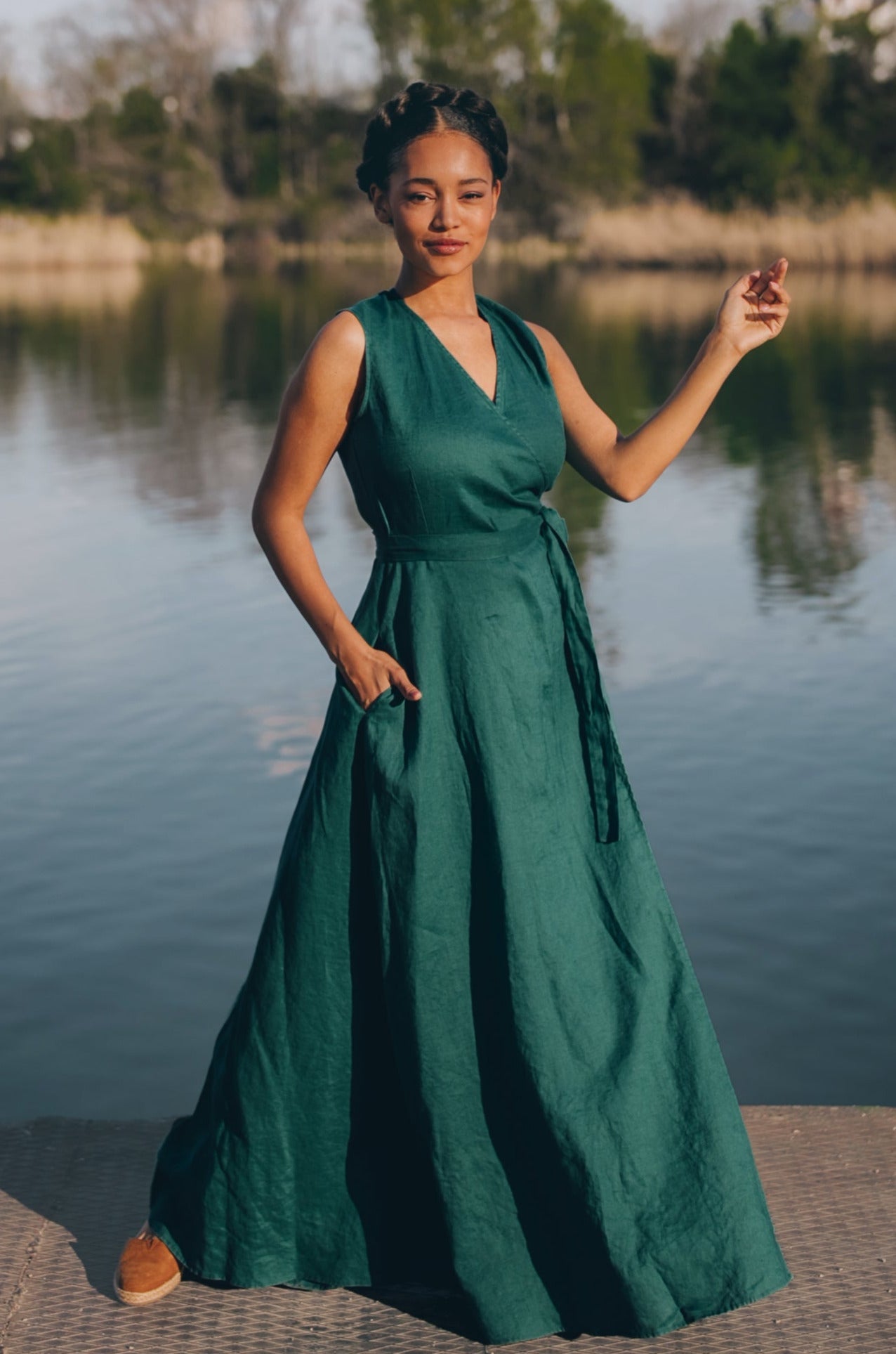 Woman wearing sleeveless green linen maxi dress with tie waist standing by a lake