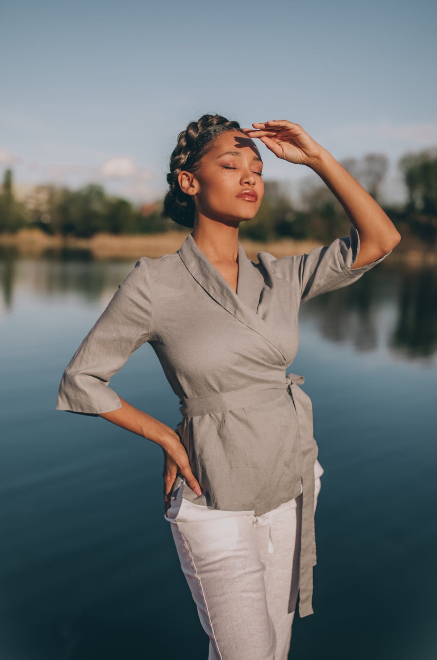 Woman wearing grey linen wrap top with shawl neck and elbow sleeves by the lake