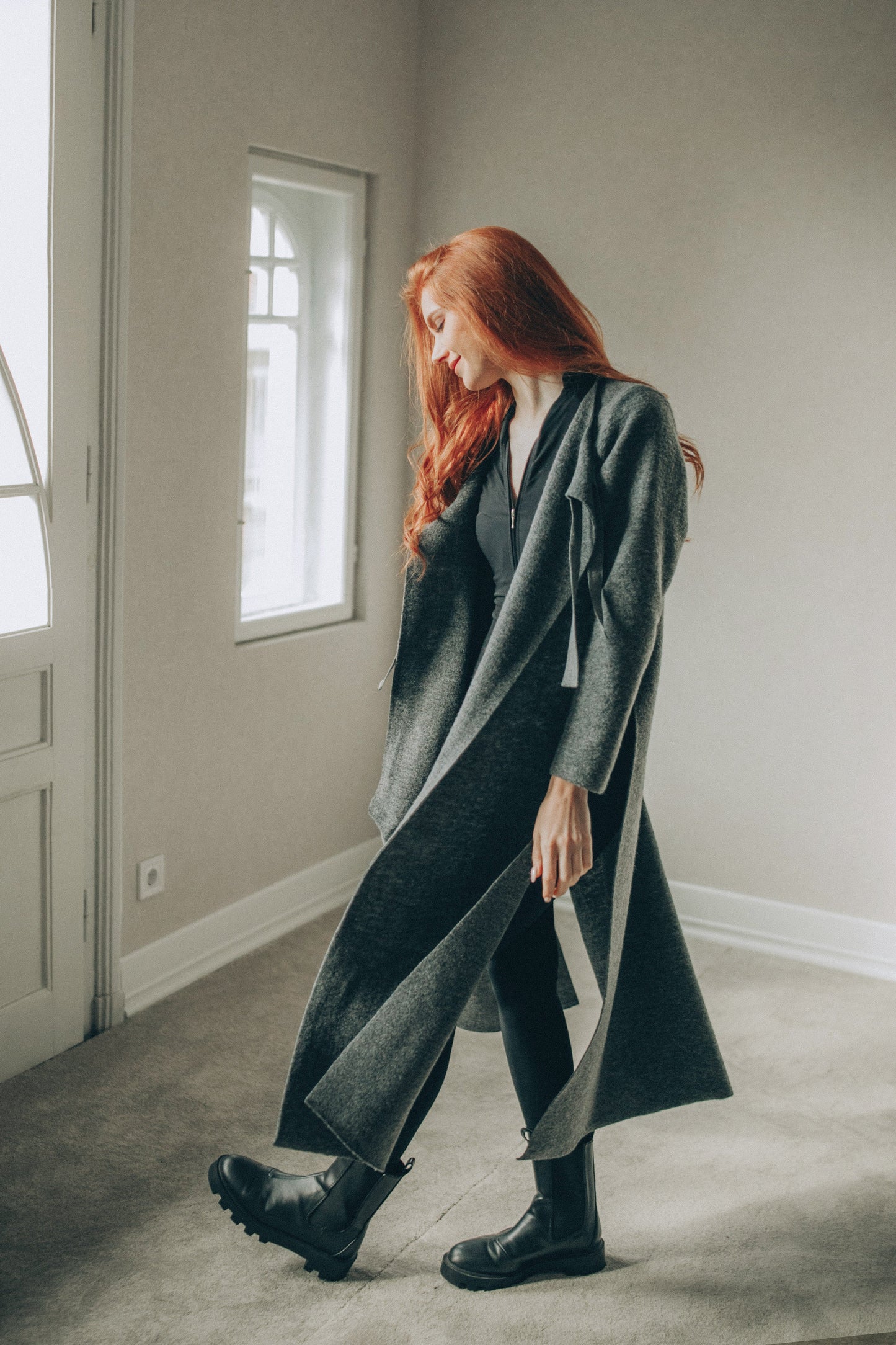 Woman wearing a long dark gray cardigan in a minimalistic room.