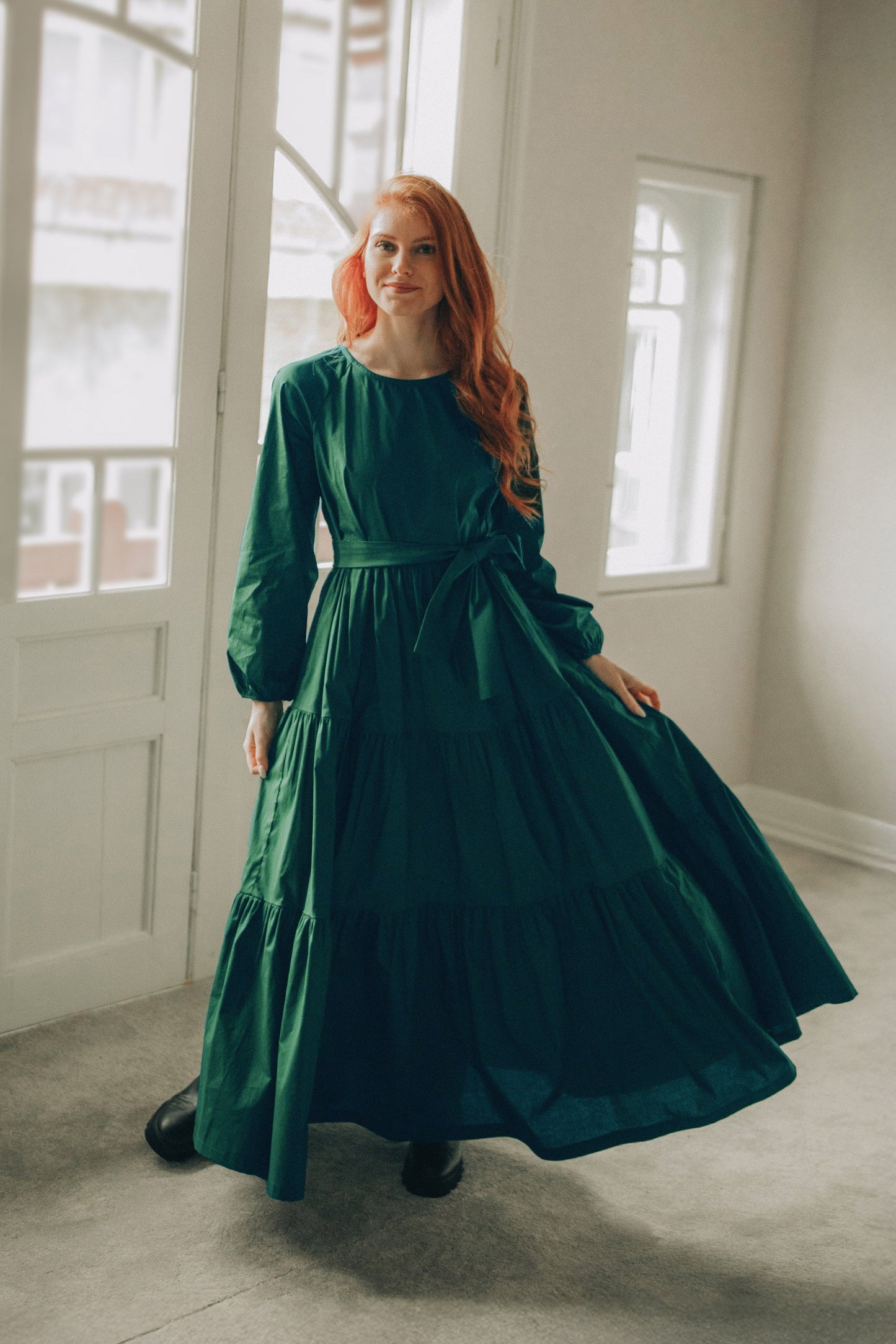 woman wearing green tiered cotton maxi dress with long sleeves and tie waist standing indoors