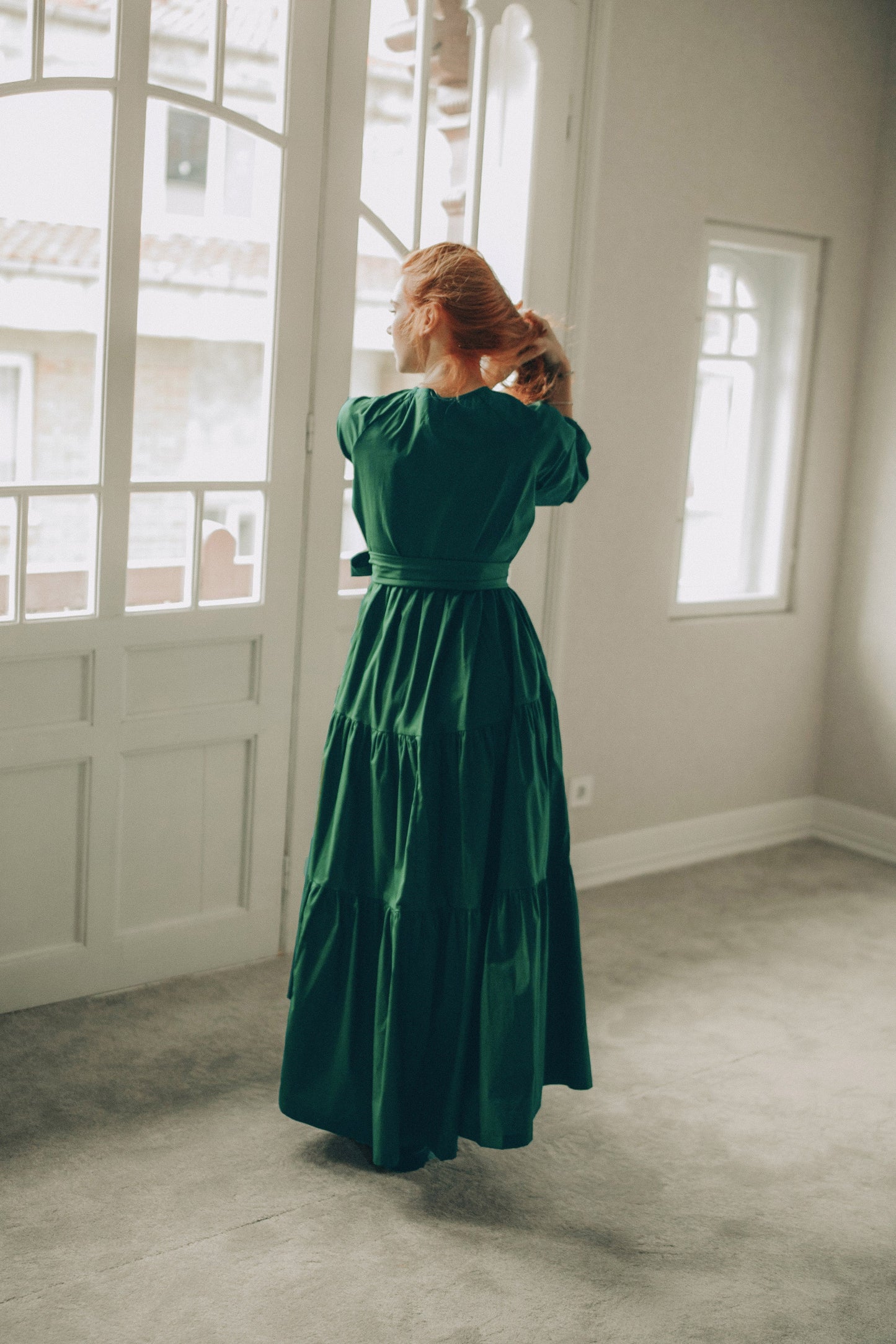 Woman in a green dress standing in a room with large windows.