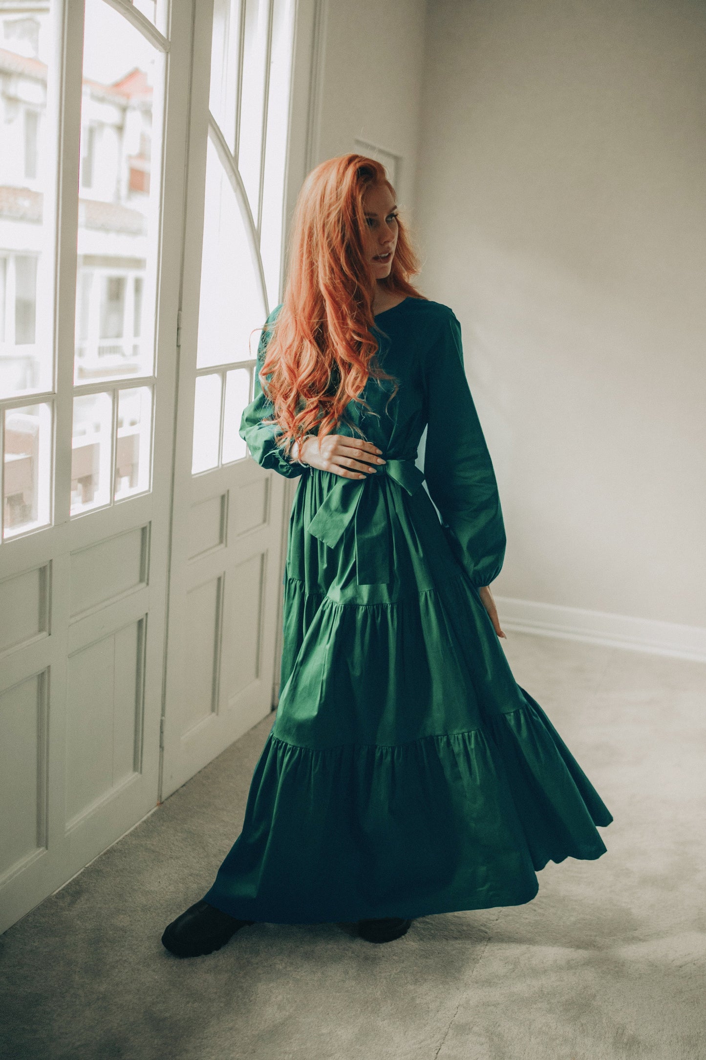 Woman in a green dress standing in a room with large windows.