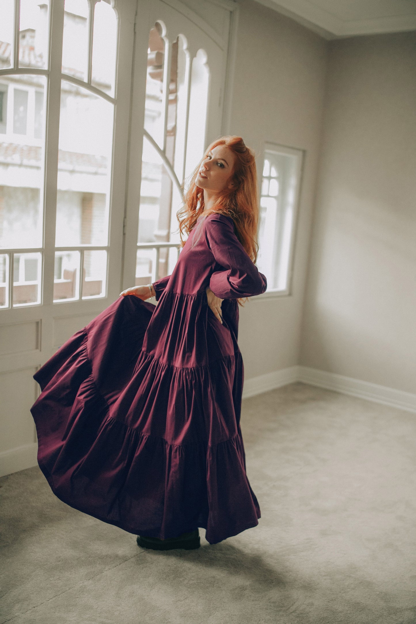 Woman in a long, dark purple dress standing in a room with large windows.