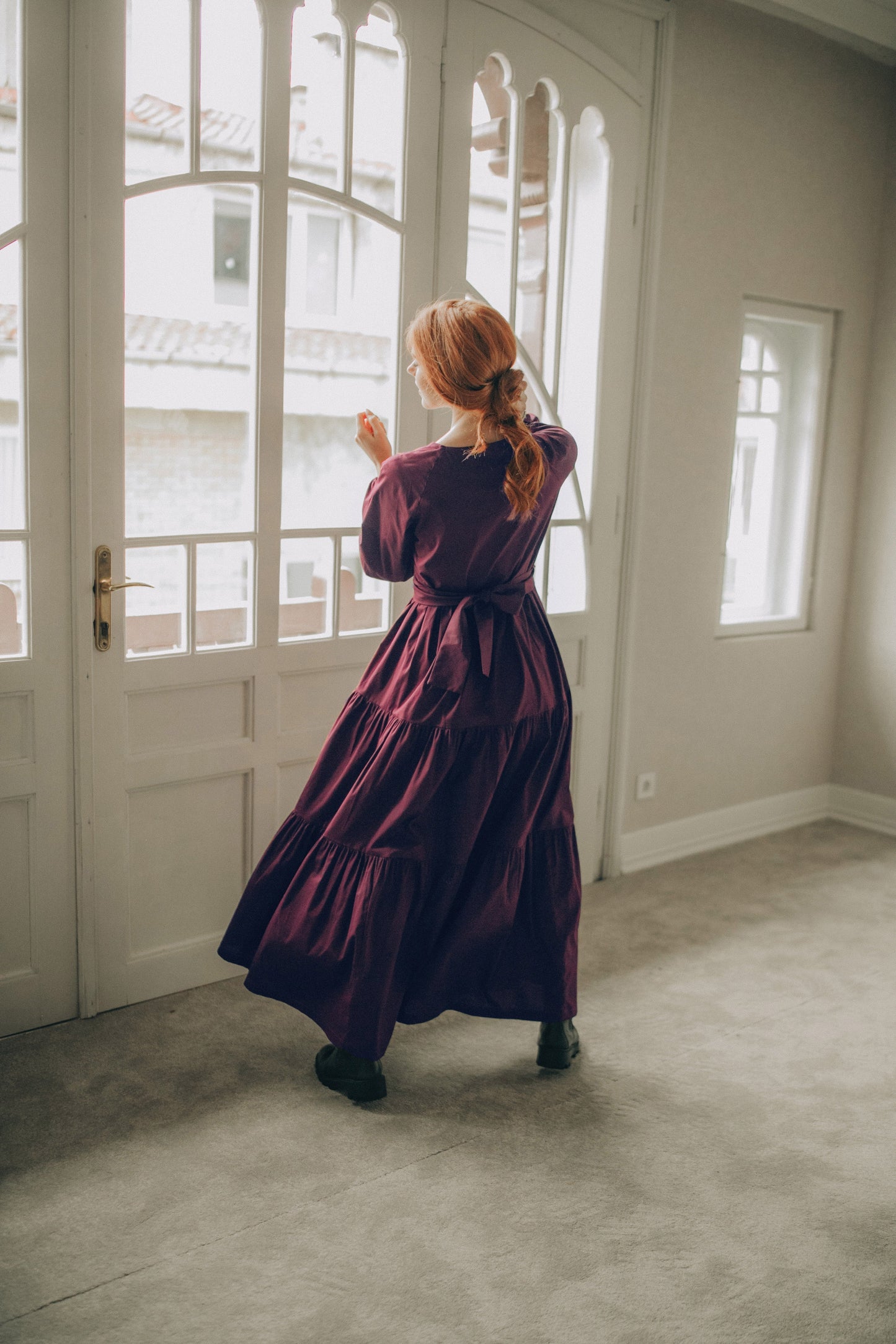 Woman in a long purple dress standing in a room with large windows.