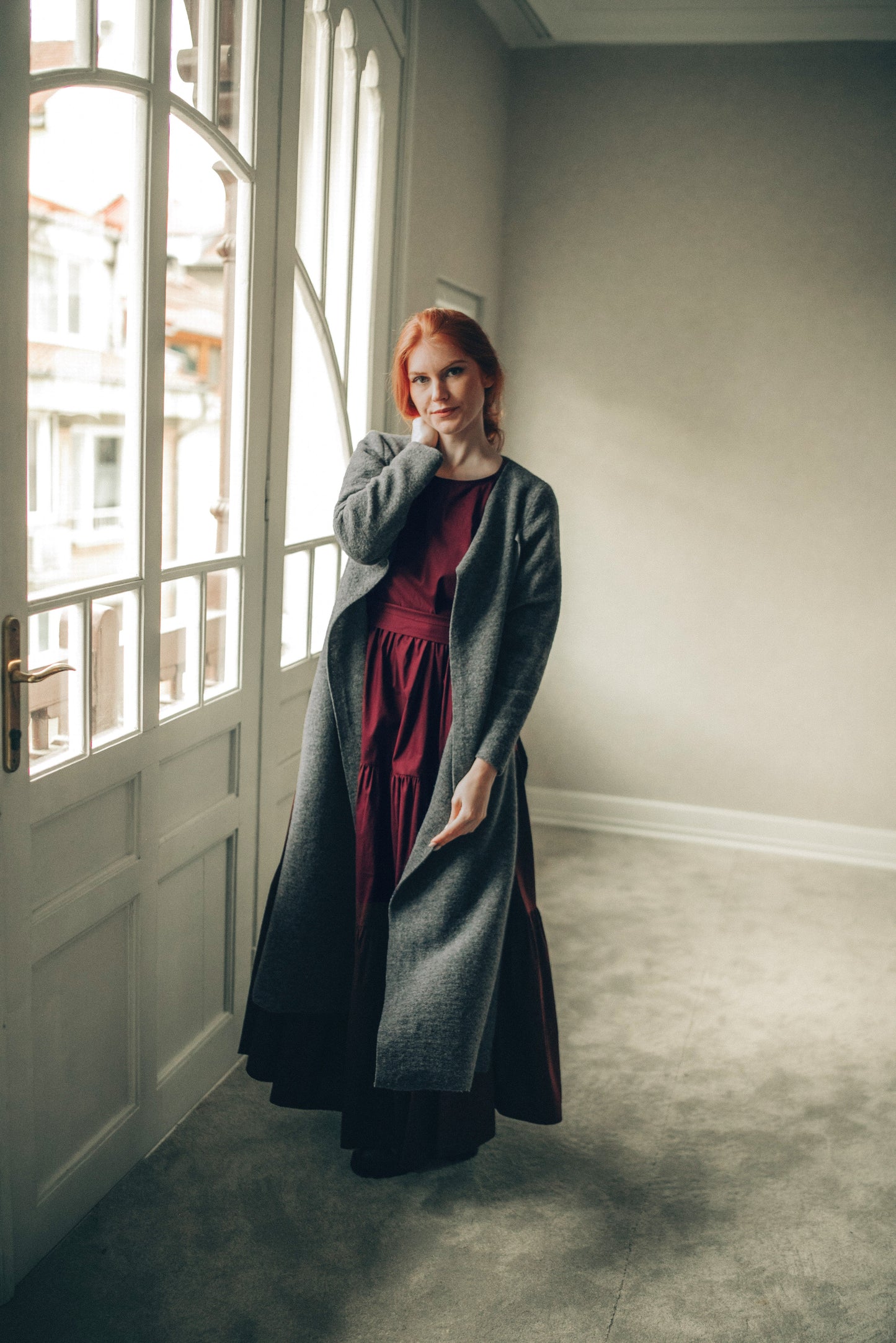 Woman wearing a long dark gray cardigan in a minimalistic room.