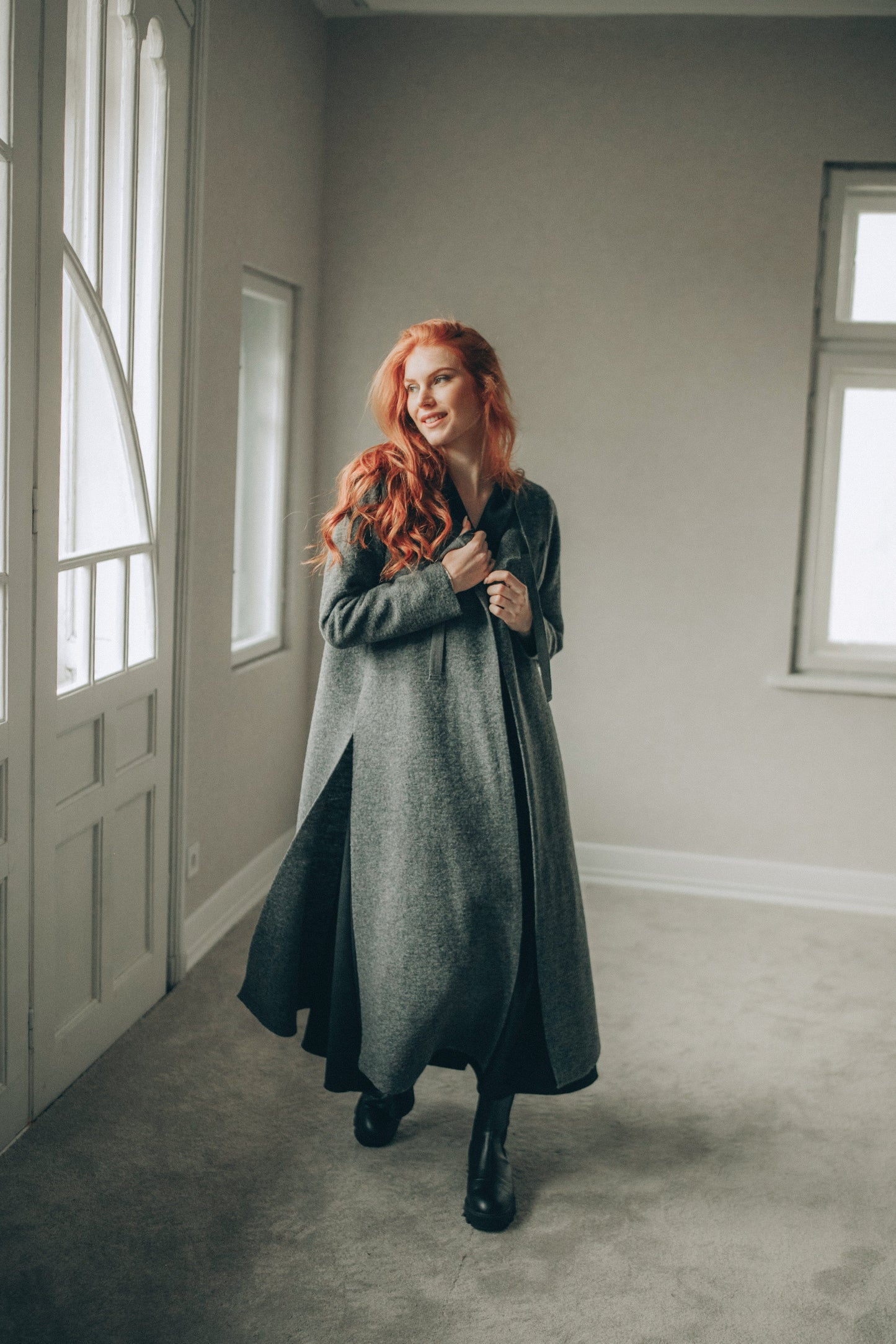Woman with red hair standing in a room with neutral walls and a door.