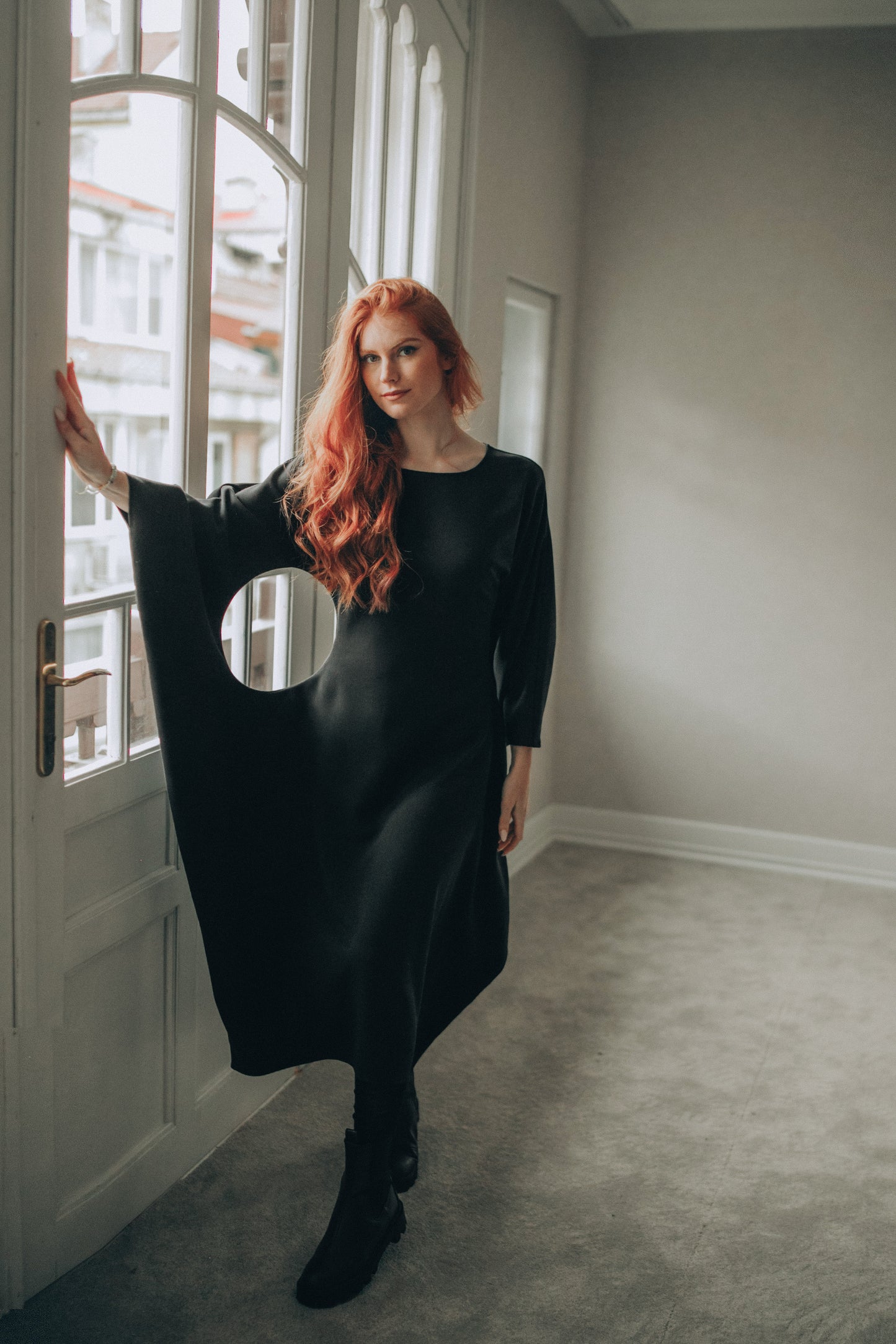 Woman in a black dress standing in a room with large windows.