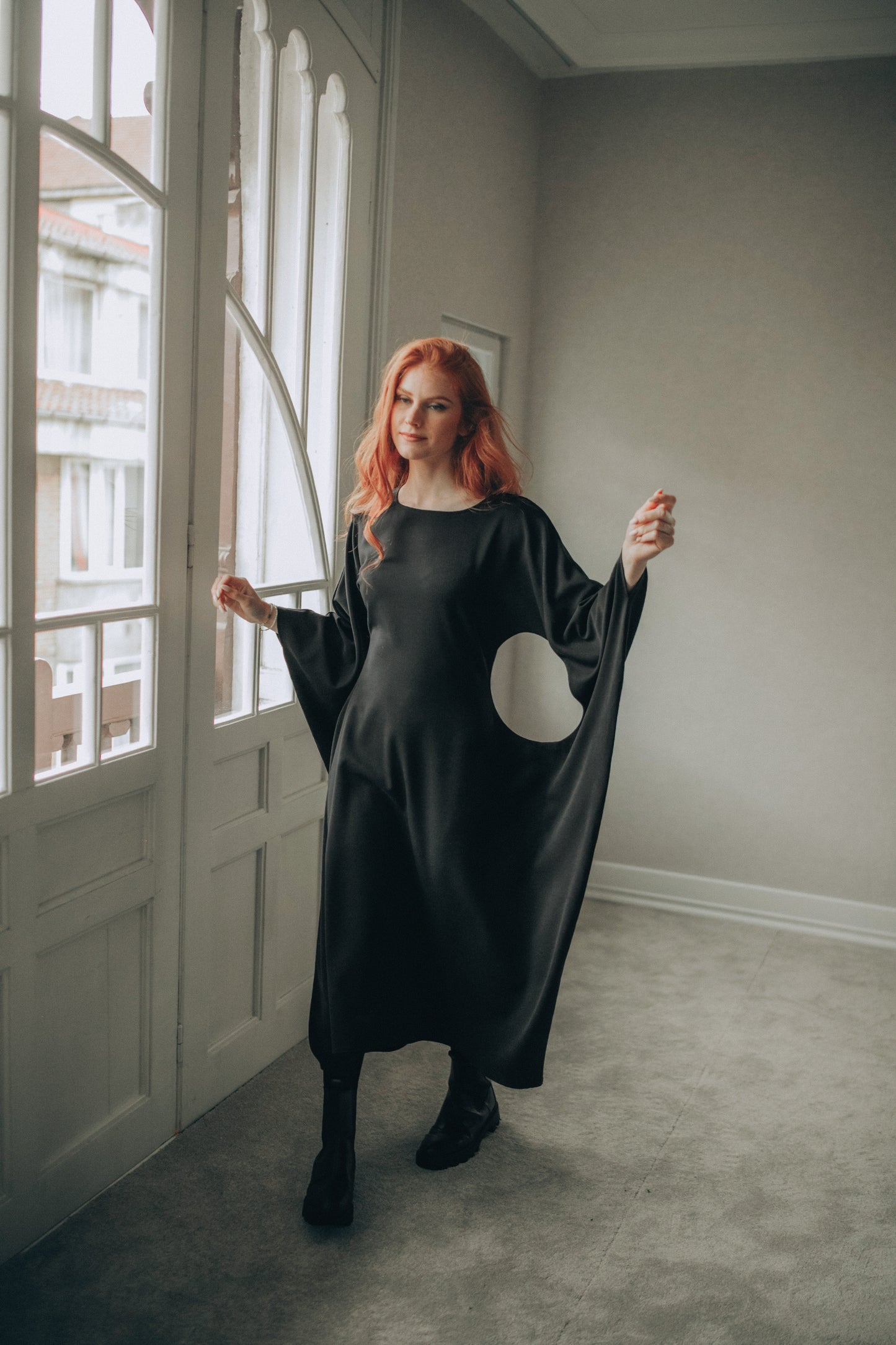 Woman wearing a black midi dress with a moon design in a room with large windows.