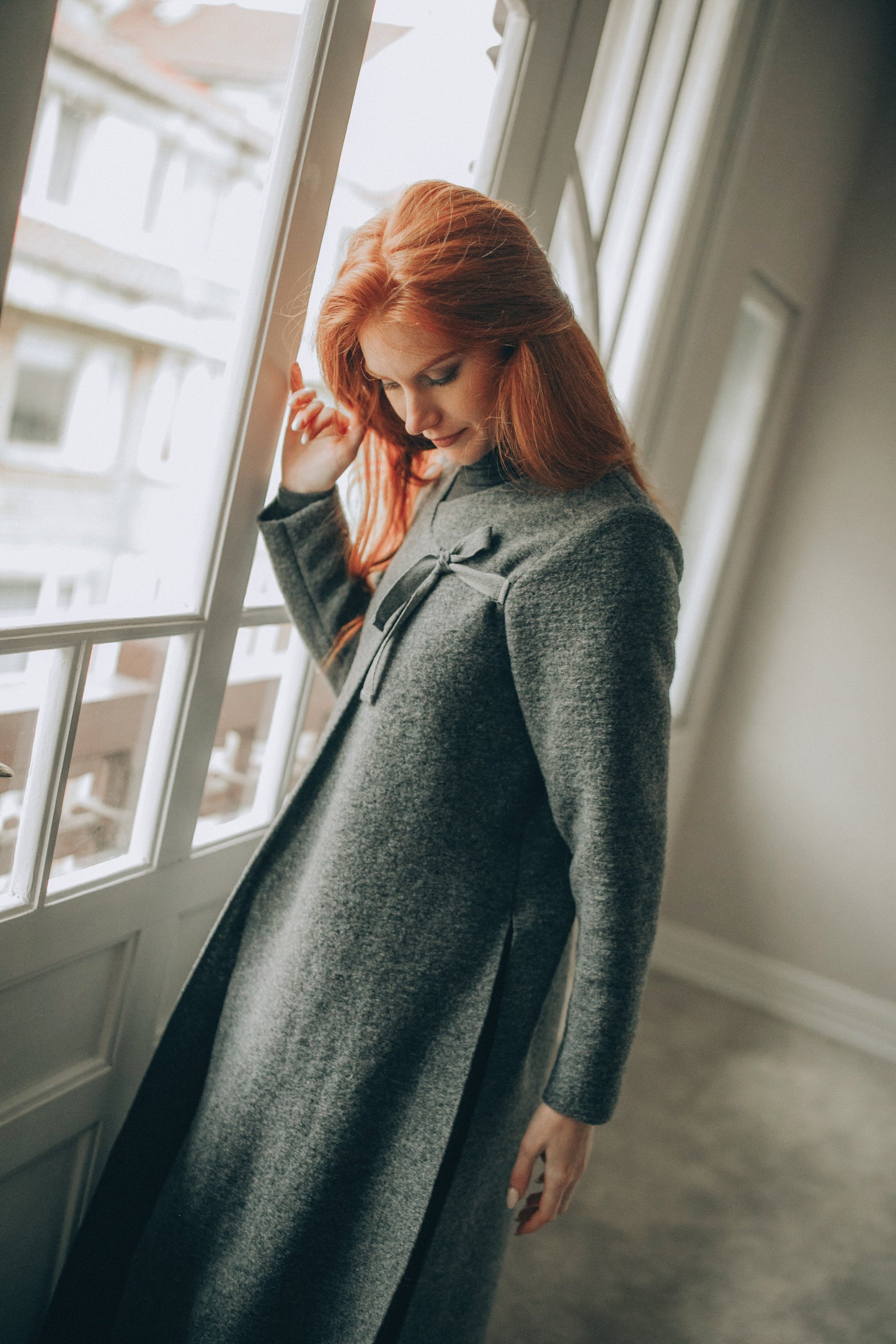 Woman wearing a long dark gray cardigan in a minimalistic room.