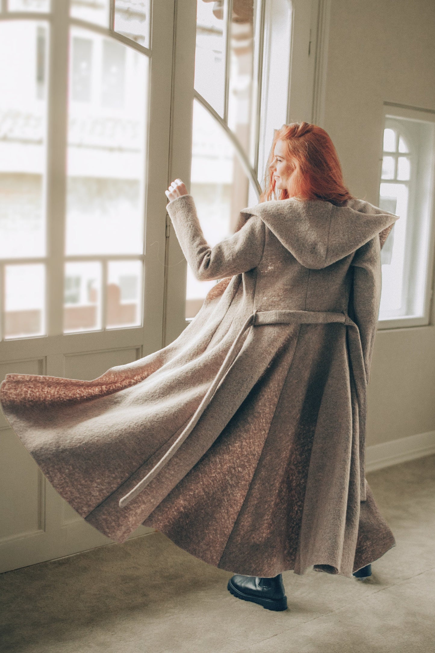 Maxi wool hooded cardigan coat with princess silhouette and adjustable belt, flowing long skirt, cozy hood, and deep pockets, worn indoors.