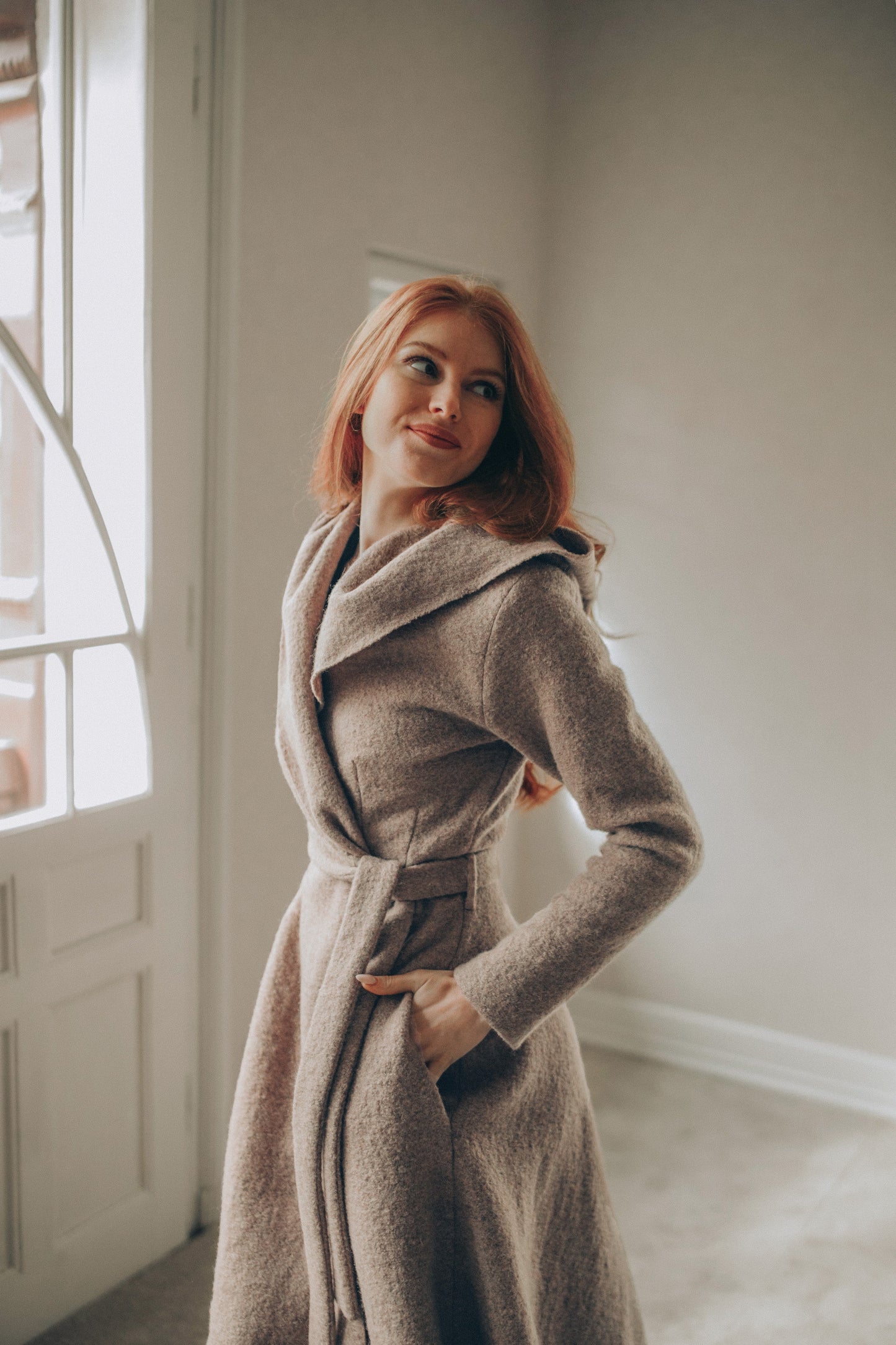 Woman in a Maxi Wool Hooded Cardigan Coat standing in a room with large windows.