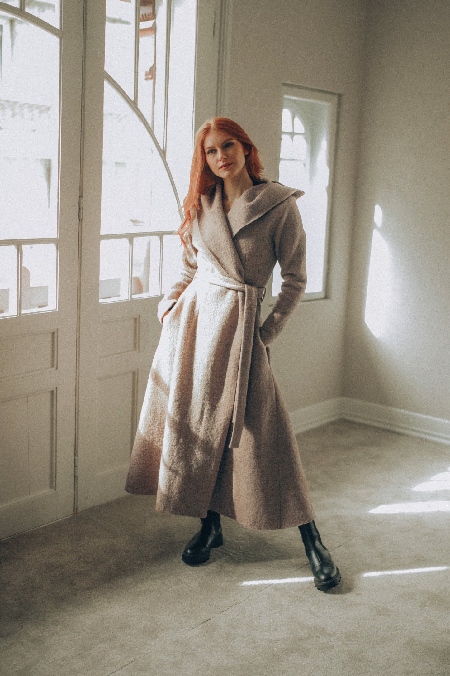 Woman in a Maxi Wool Hooded Cardigan Coat standing in a room with large windows.