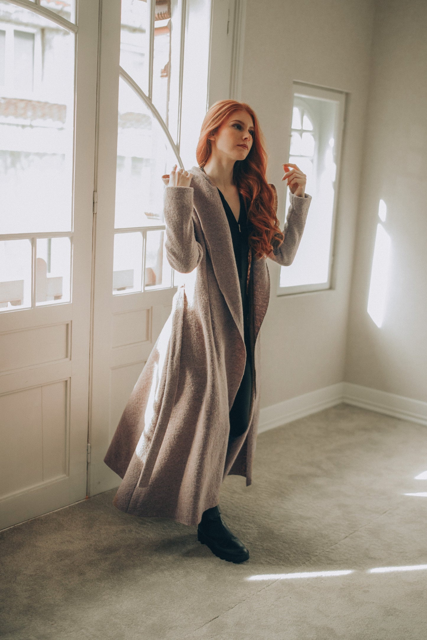 Woman in a Maxi Wool Hooded Cardigan Coat standing in a room with large windows.