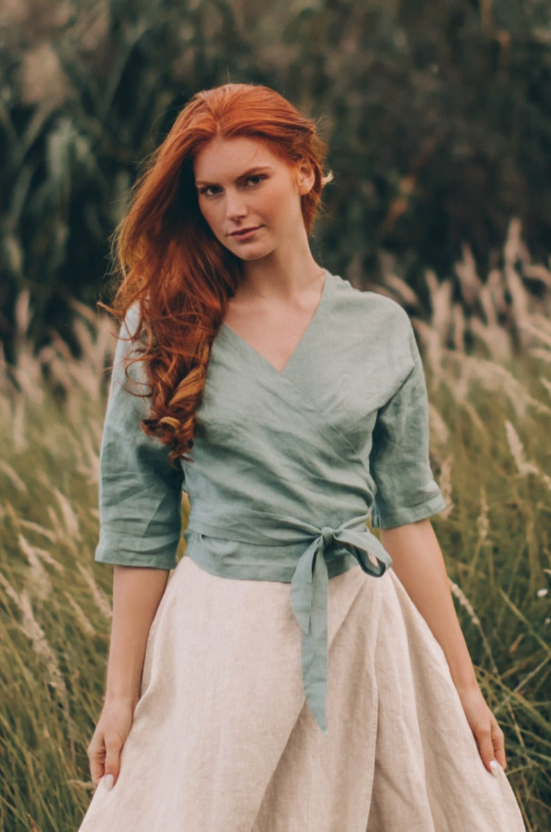 Woman wearing minimalist linen wrap top with elbow-length sleeves and tie closure in outdoor natural setting