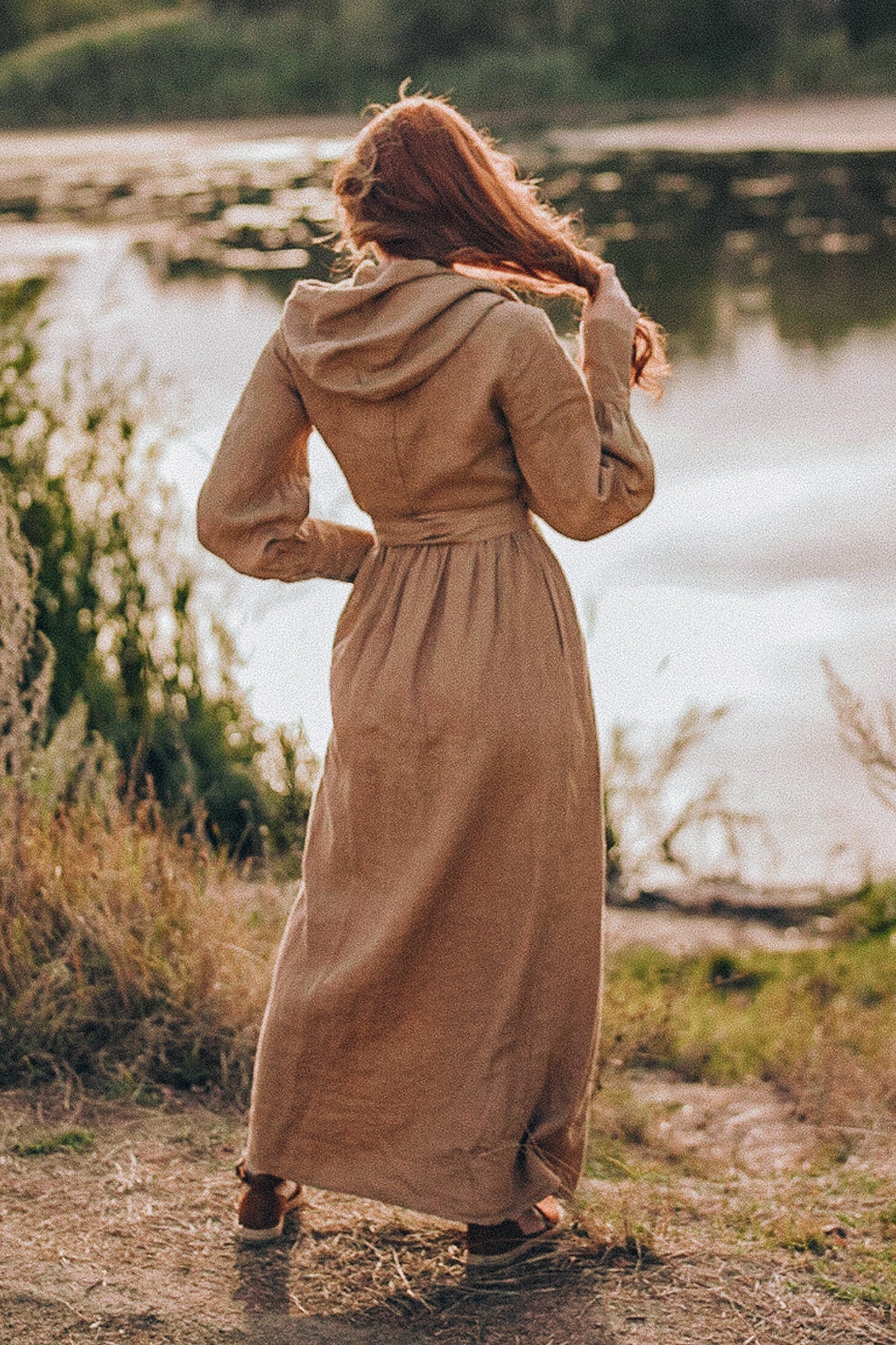 Woman wearing camel maxi linen wrap dress with a hood standing outdoors near water