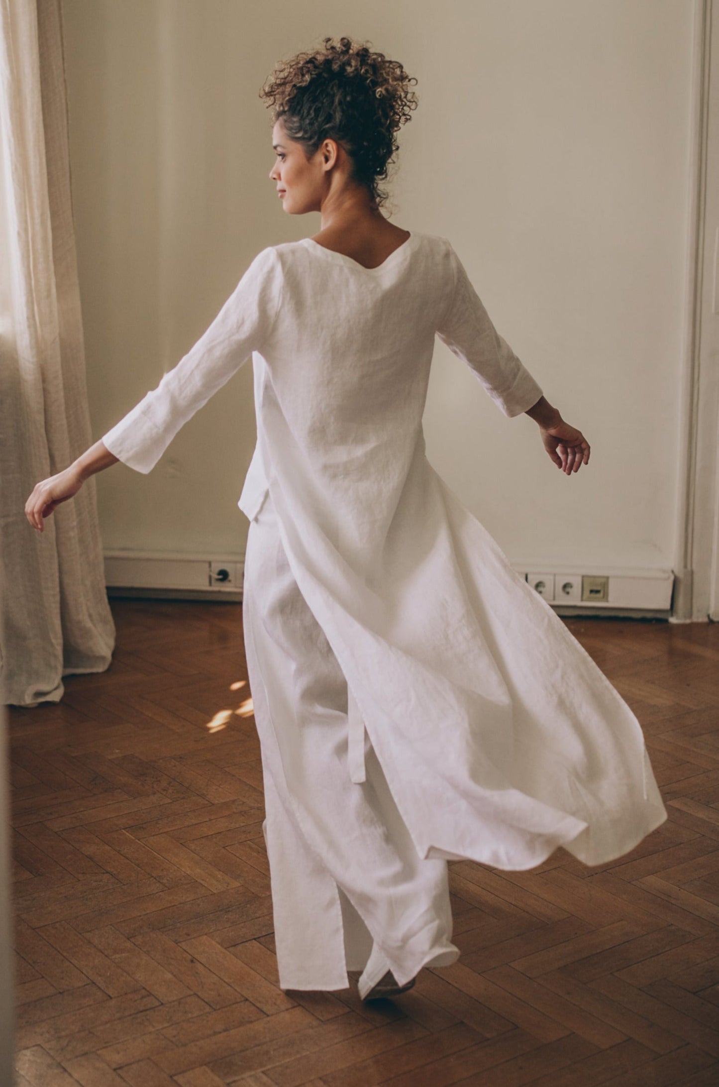 Woman wearing white asymmetric tunic shirt with long back made of linen indoors