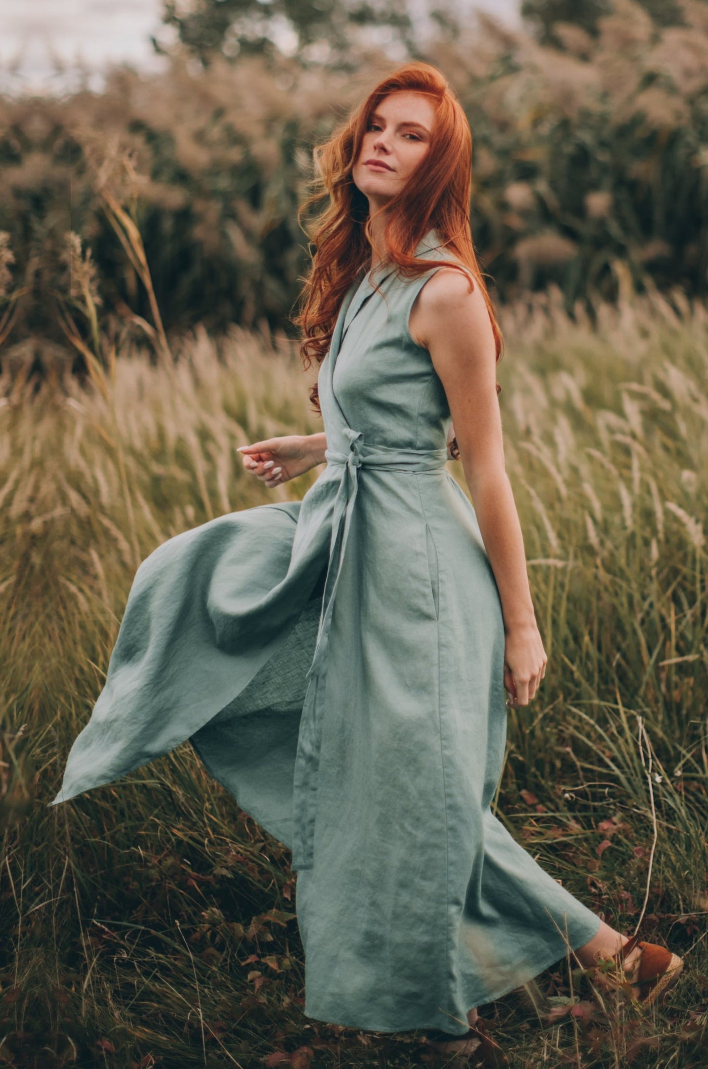 Woman wearing sleeveless linen wrap dress with tie waist standing in a field of tall grass