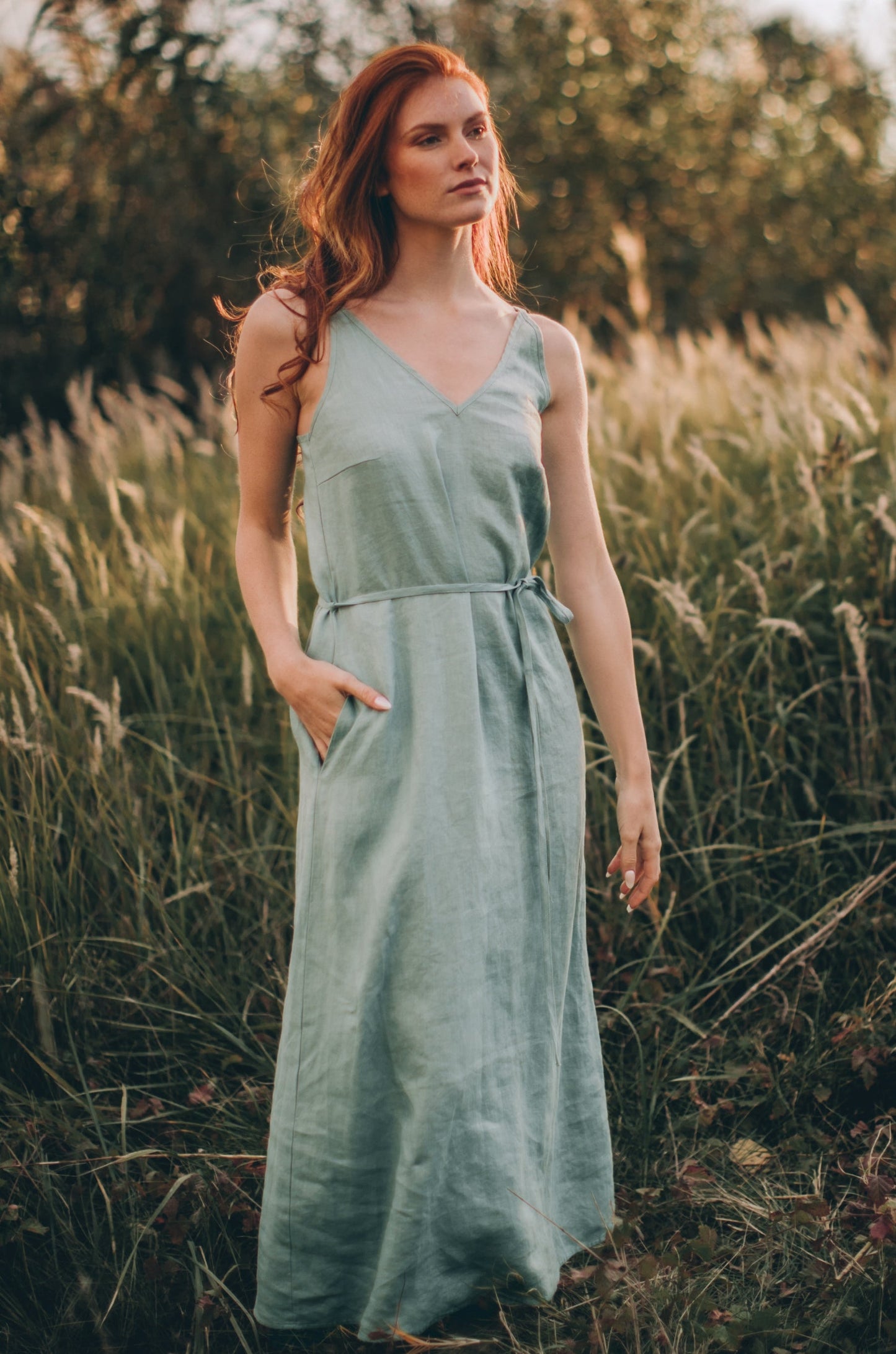Woman wearing dusty turquoise linen slip dress with adjustable straps and tie belt outdoors